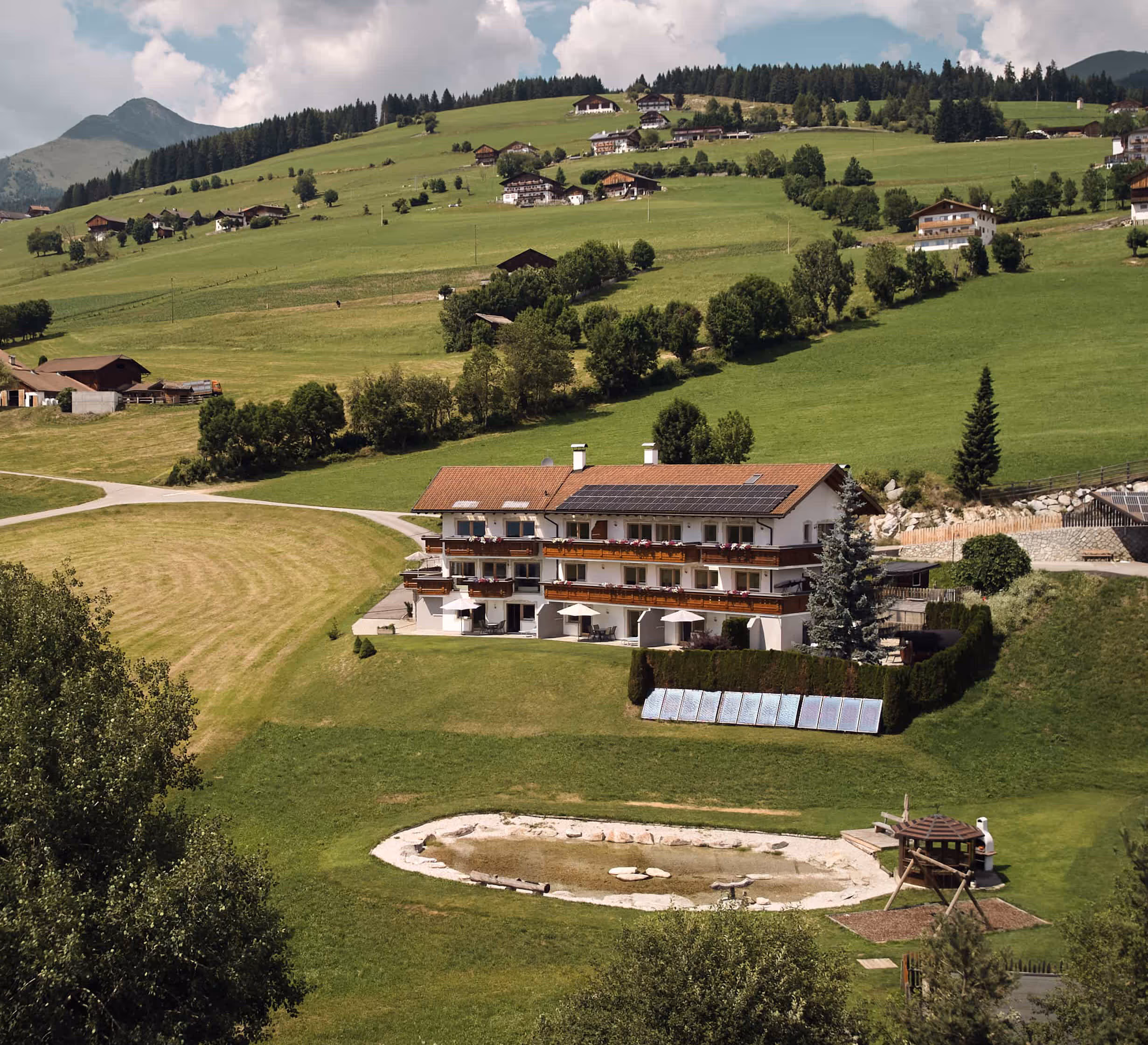 Marketingprojekt Bergdiamant: Panoramaaufnahme eines Hotels in grüner Hügellandschaft mit Solarpanels und kleinem Naturteich im Vordergrund.