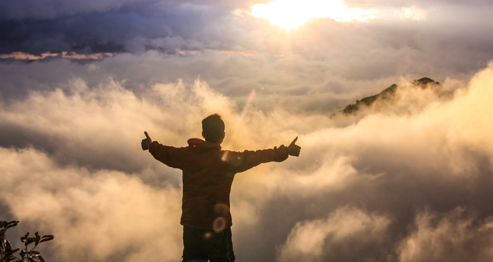 man with both thumbs up at the top of a mountain