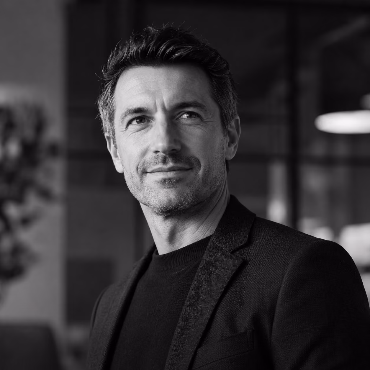 Black and white portrait of a confident man wearing a blazer looking slightly right with a soft smile.