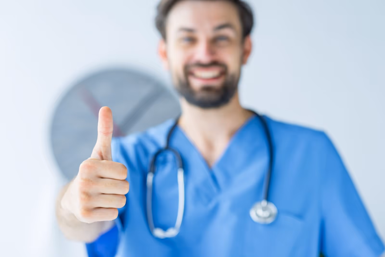 Smiling doctor in blue scrubs giving thumbs up in medical clinic setting