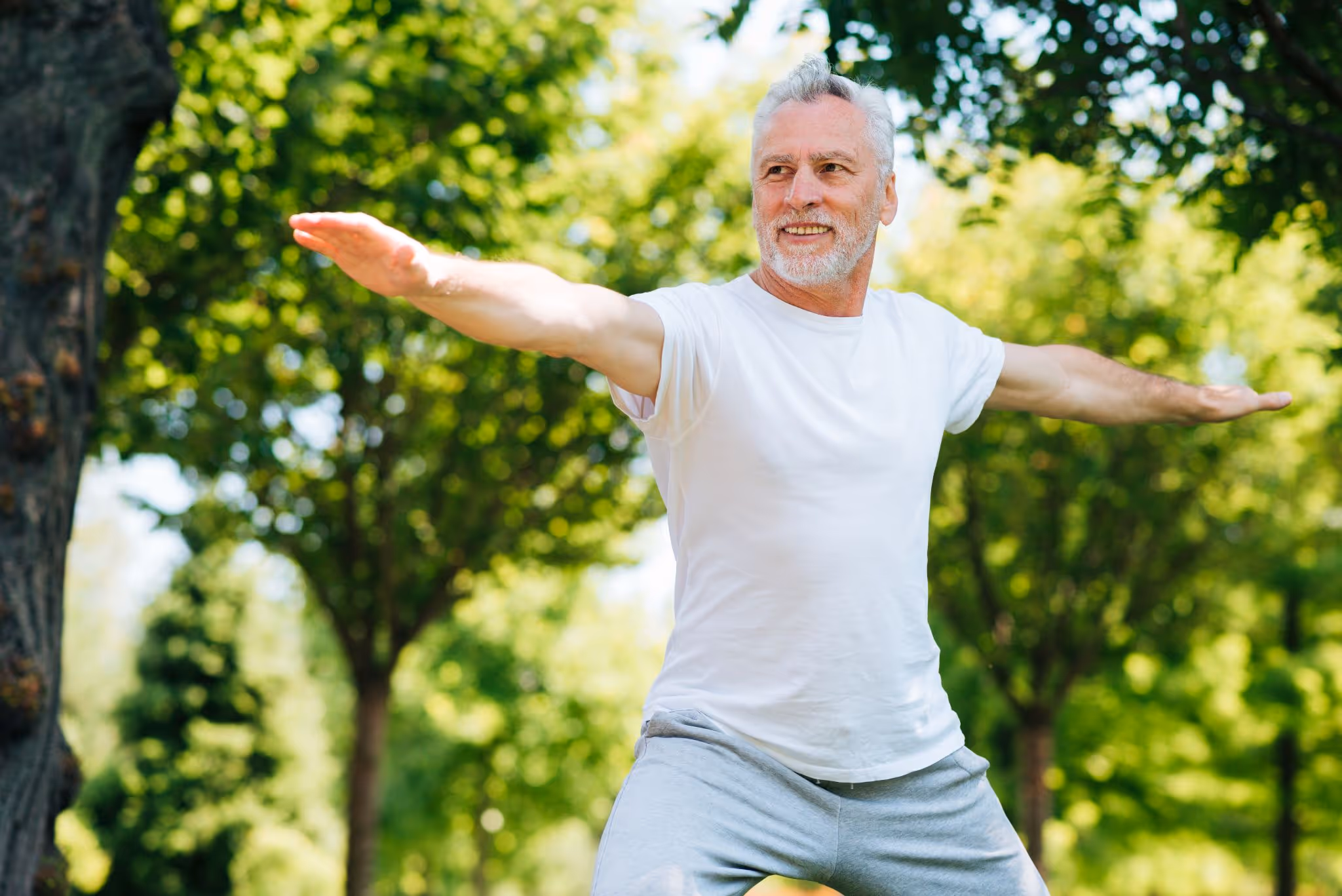 Active senior man over 50 with gray hair doing stretching exercise outdoors, demonstrating vitality and energy