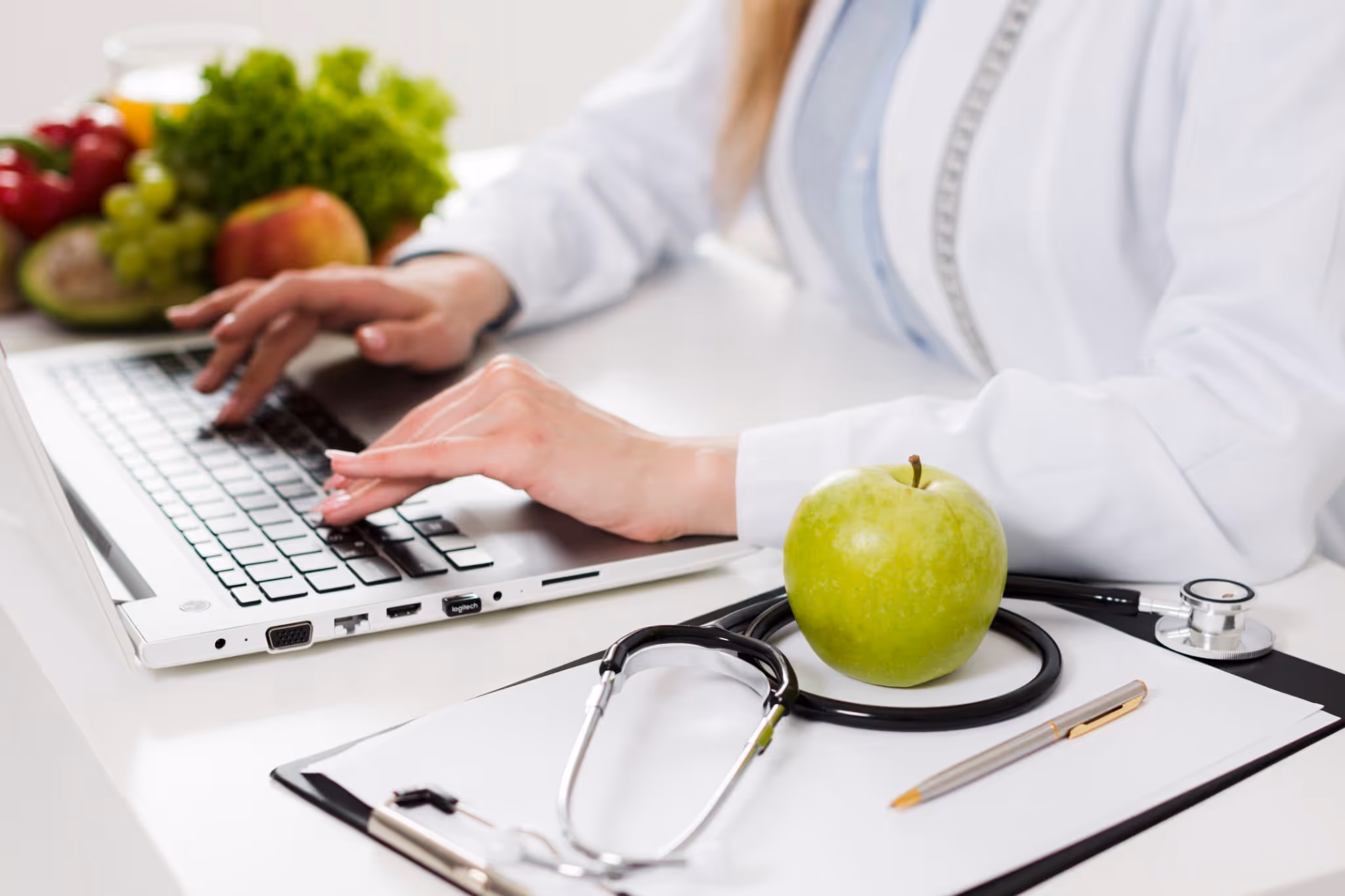 Doctor typing on laptop with stethoscope and green apple promoting healthy lifestyle