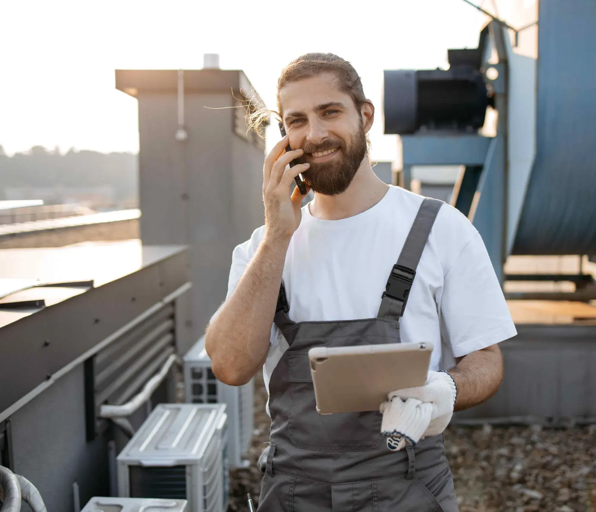 HVAC technician on a rooftop taking an emergency call and updating Jobber on a tablet