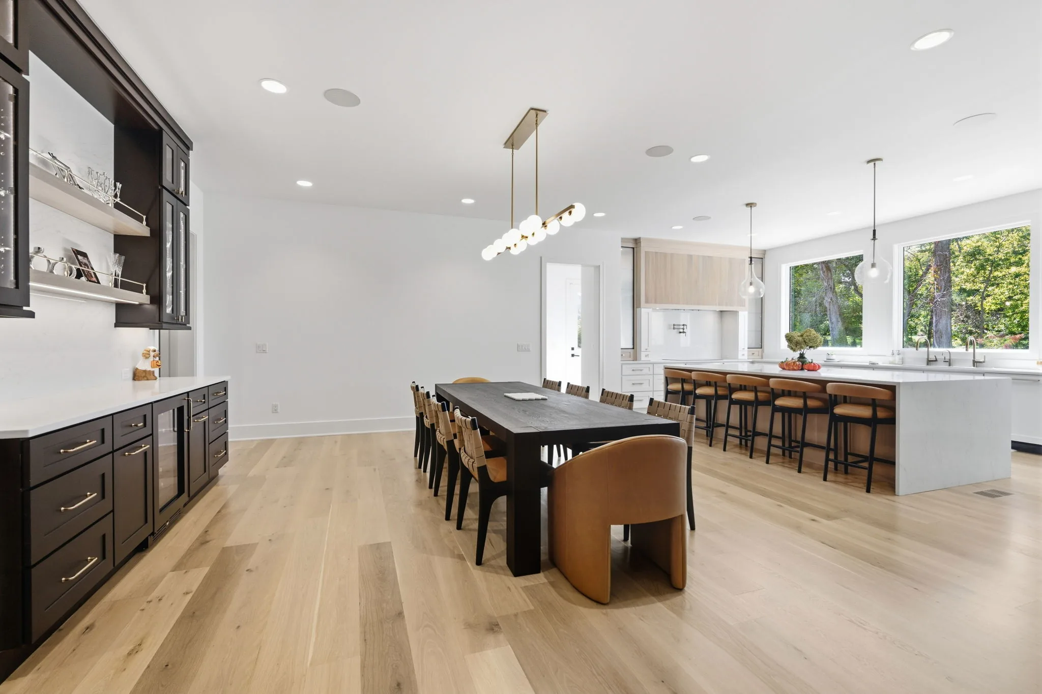 Dining area with a brass linear chandelier and dry bar beside a kitchen with a waterfall island