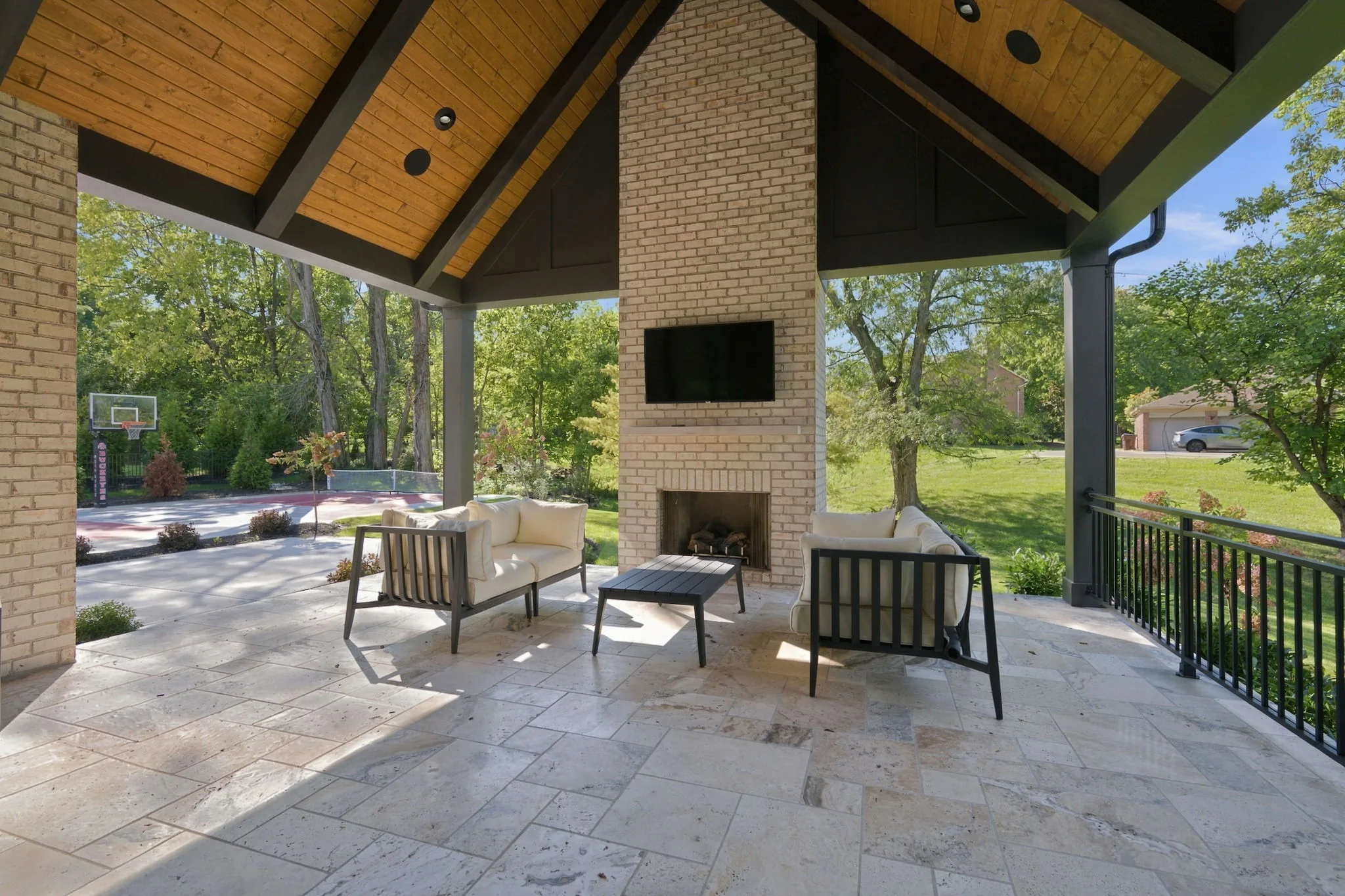 Covered rear porch with a wood-plank ceiling, brick fireplace, and stone floor