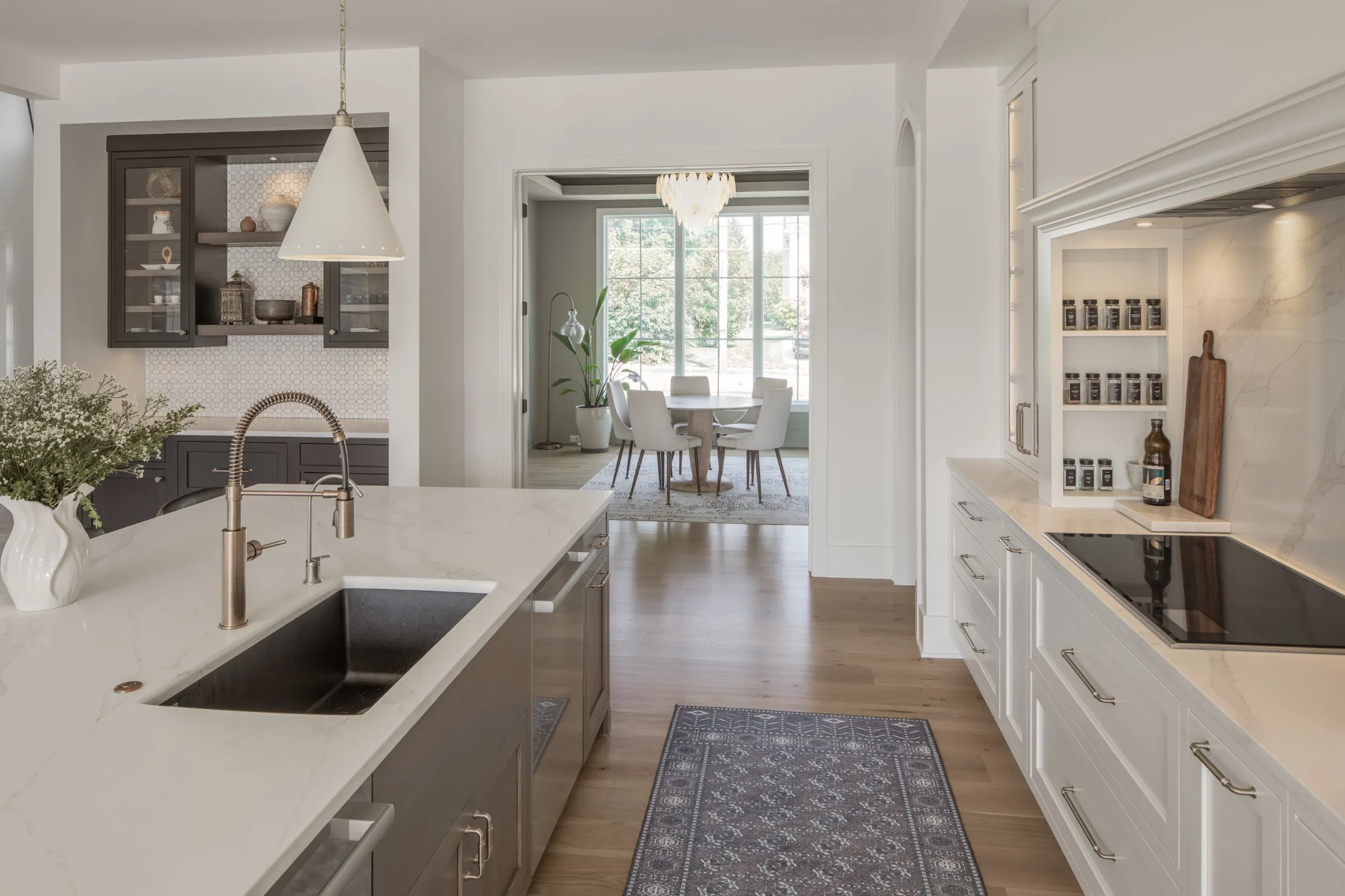Kitchen with a dark-stained island and undermount sink, looking into a breakfast room with tall windows