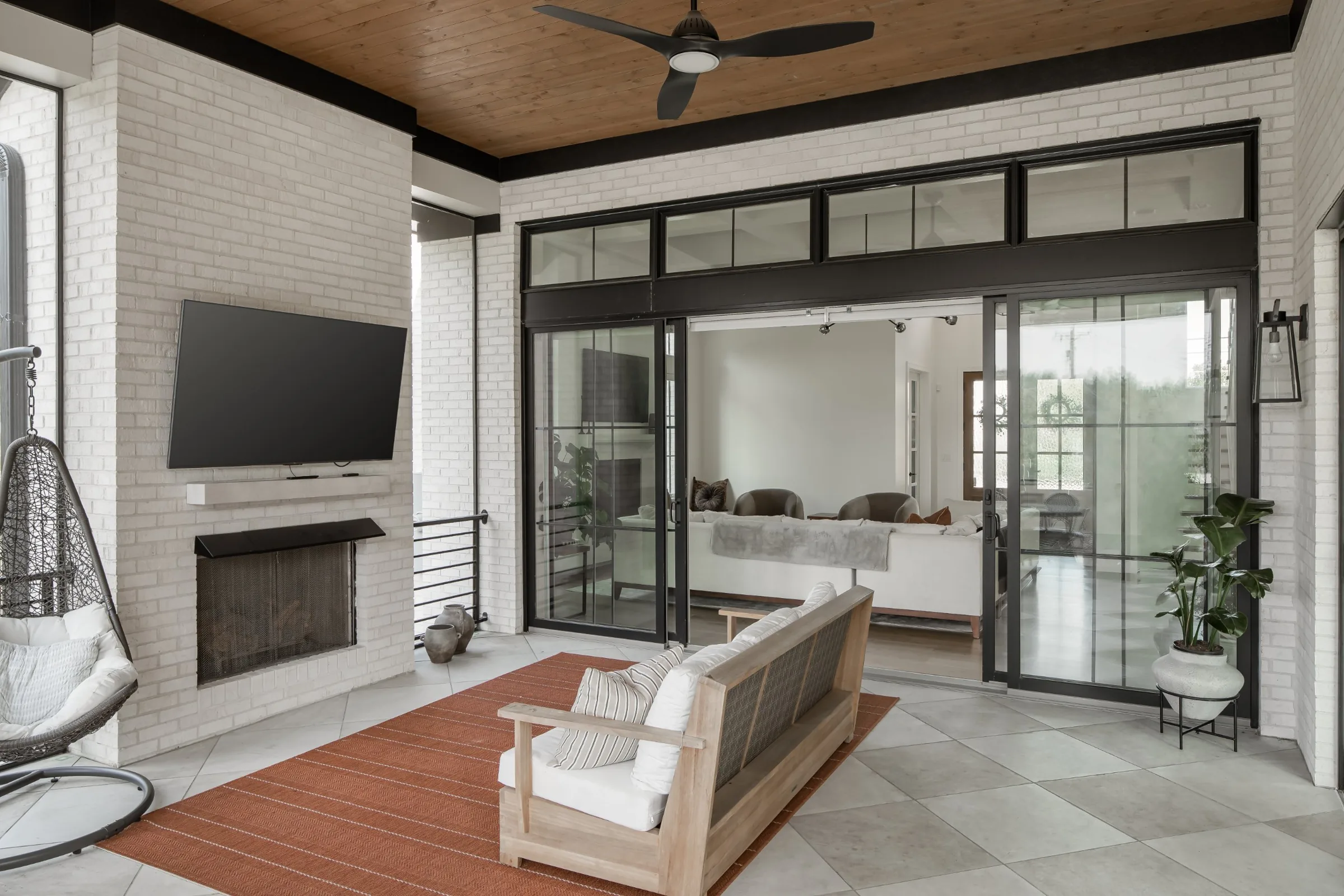 Covered porch with a brick fireplace and black-framed sliding doors opening to the family room
