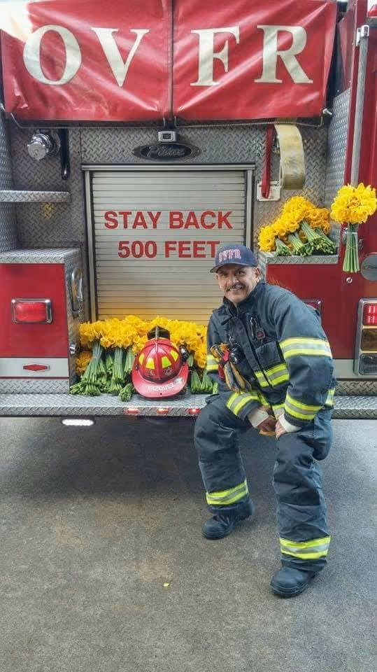 Captain Arthur A. Vazquez sitting on the back of a fire truck that is covered in flowers.