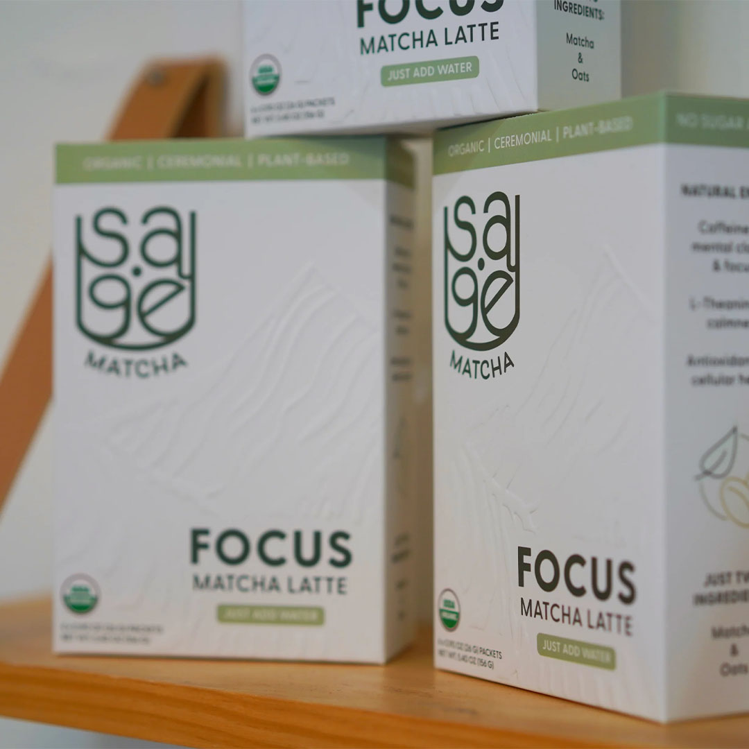 A pyramid-shaped stack of three Sage Matcha Focus blend boxes on a wooden shelf.