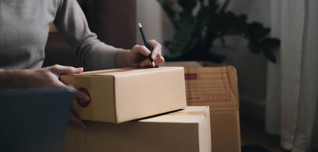 a man writing on a cardboard moving box with a pencil