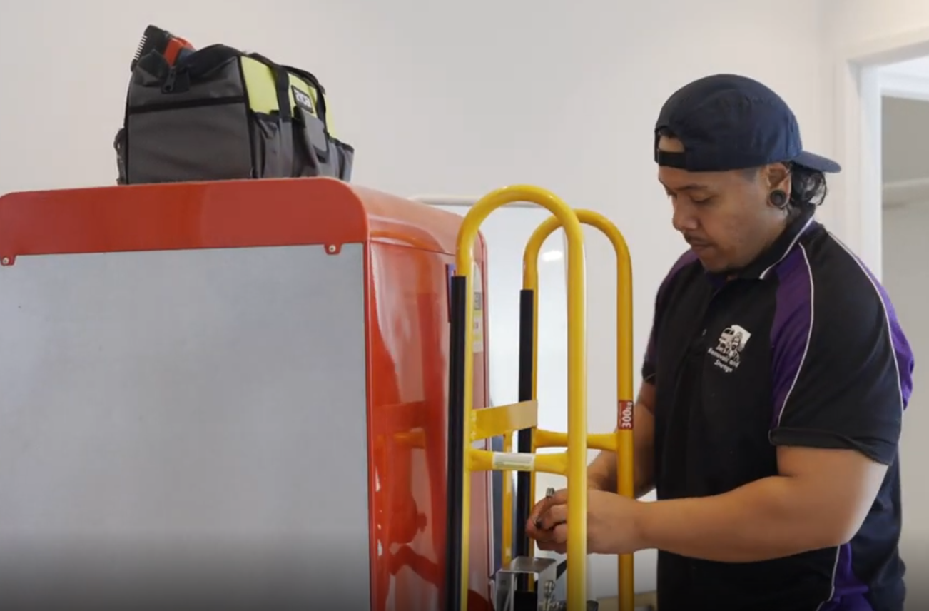 Jim's Removals mover loading a red fridge onto a yellow moving trolley.