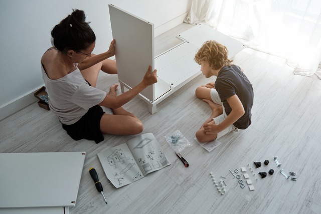 Mother and son reassembling a white cabinet with instructions.