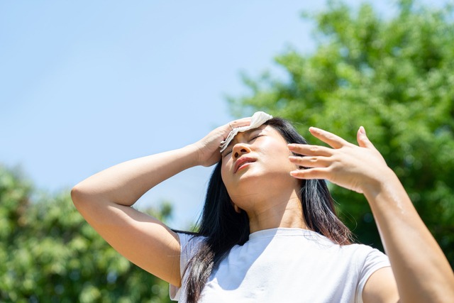 Woman sweating outdoors with a towel to her forehead