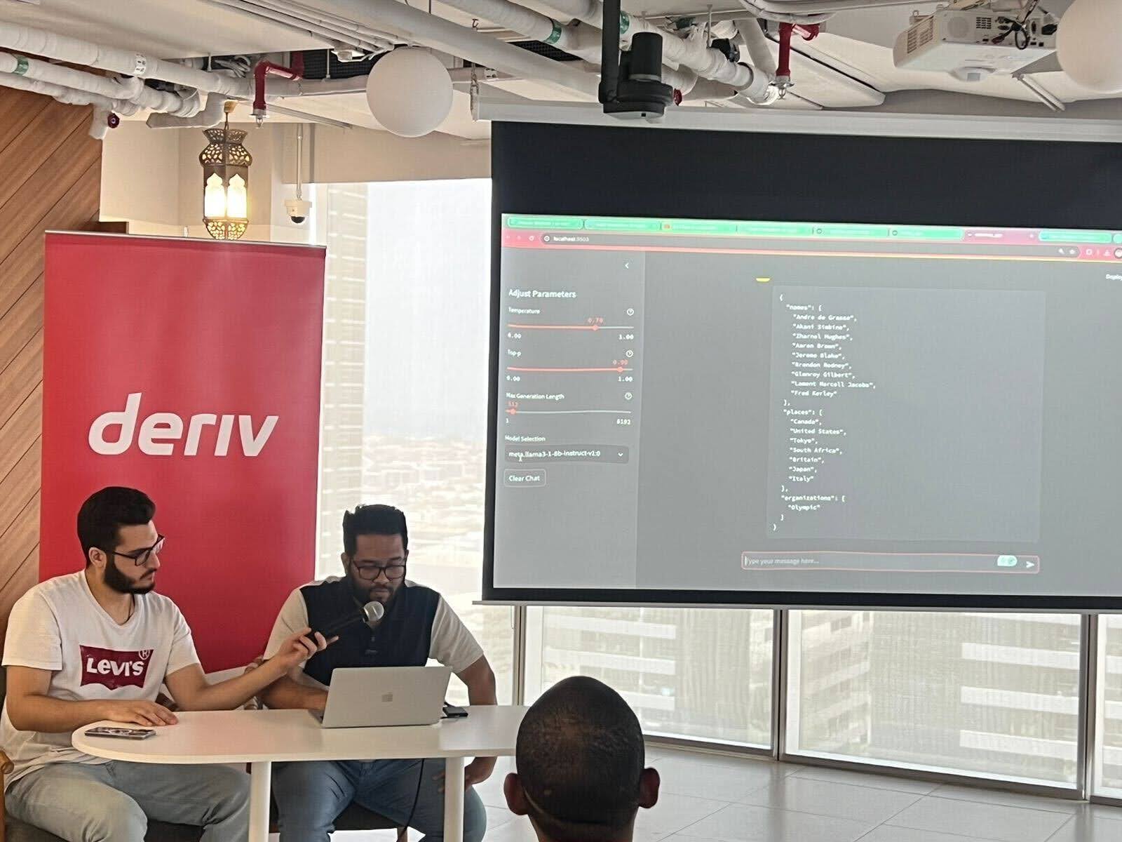 Deriv host holds a microphone while the AWS speaker presents on a laptop during an AWS community event.