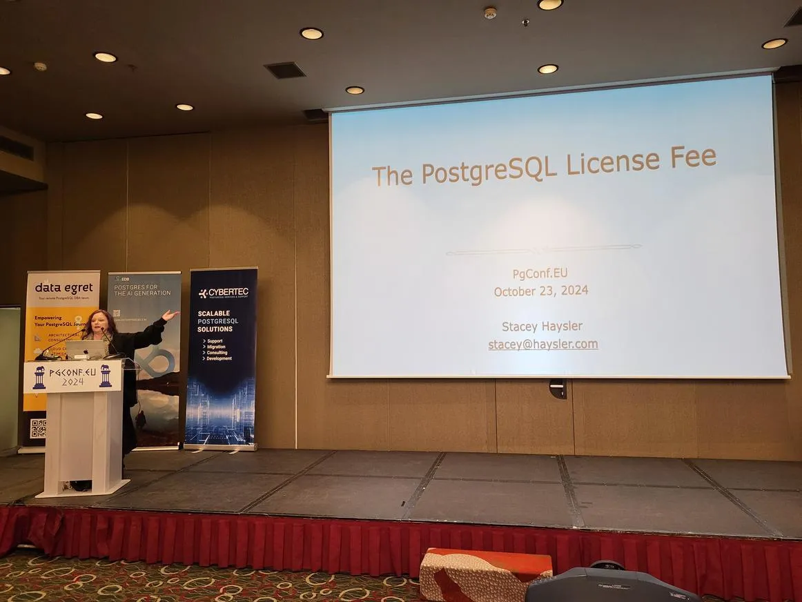 Stacey Haysler presenting 'The PostgreSQL License Fee' at PgConf.EU 2024, with sponsor banners and a slide in the background.