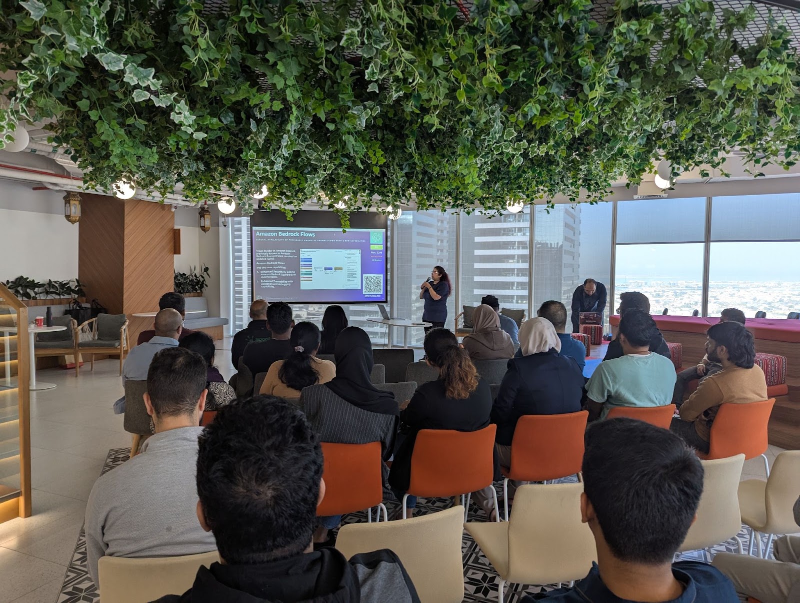 حضور في مكتب حديث يشاهدون عرضًا تقديميًا عن Amazon Bedrock Flows، مع متحدث يشرح بنية AI على شاشة كبيرة.