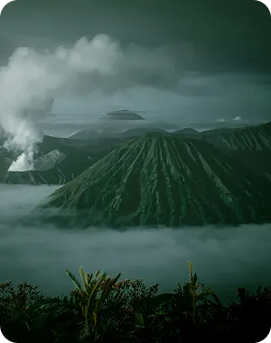 A mountain covered in fog with a plume of smoke coming out of it.