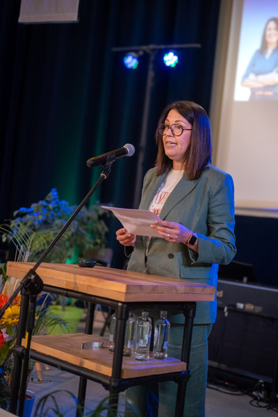 Een vrouwelijke spreker in een groen kostuum leest haar toespraak voor tijdens de academische zitting voor het 75-jarig bestaan.