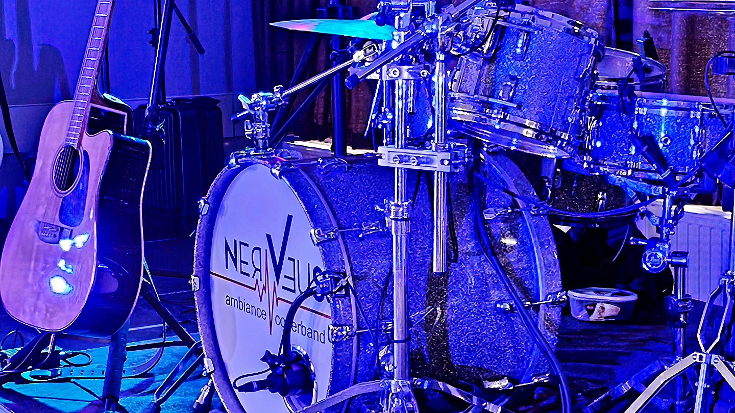 Close-up van een drumstel met het logo “Nerveus ambiance coverband”, naast een akoestische gitaar, in een blauwe belichting.