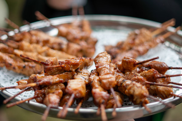Een schaal vol gegrilde kipsatés wordt geserveerd aan de bezoekers van het tuinfeest.