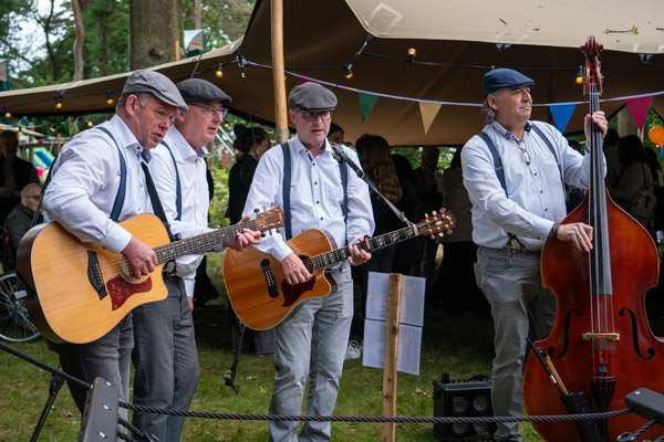 Een muzikale groep met gitaren en contrabas verzorgt live muziek in de tuin tijdens het jubileumfeest.