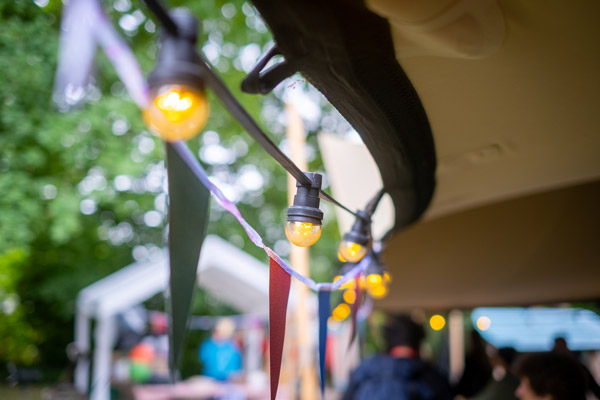 Decoratieve lichtslingers en gekleurde vlaggetjes onder een feesttent creëren een warme en gezellige sfeer tijdens het tuinfeest.