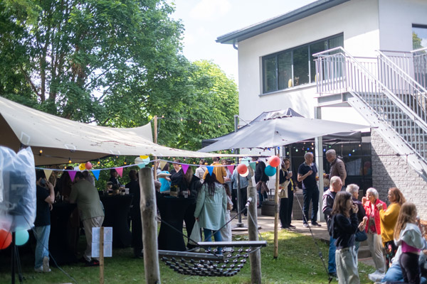 Een feestelijke buitenruimte bij het gebouw van Ons Kinderhuis met kleurrijke vlaggetjes, tenten en bezoekers die met elkaar in gesprek zijn.