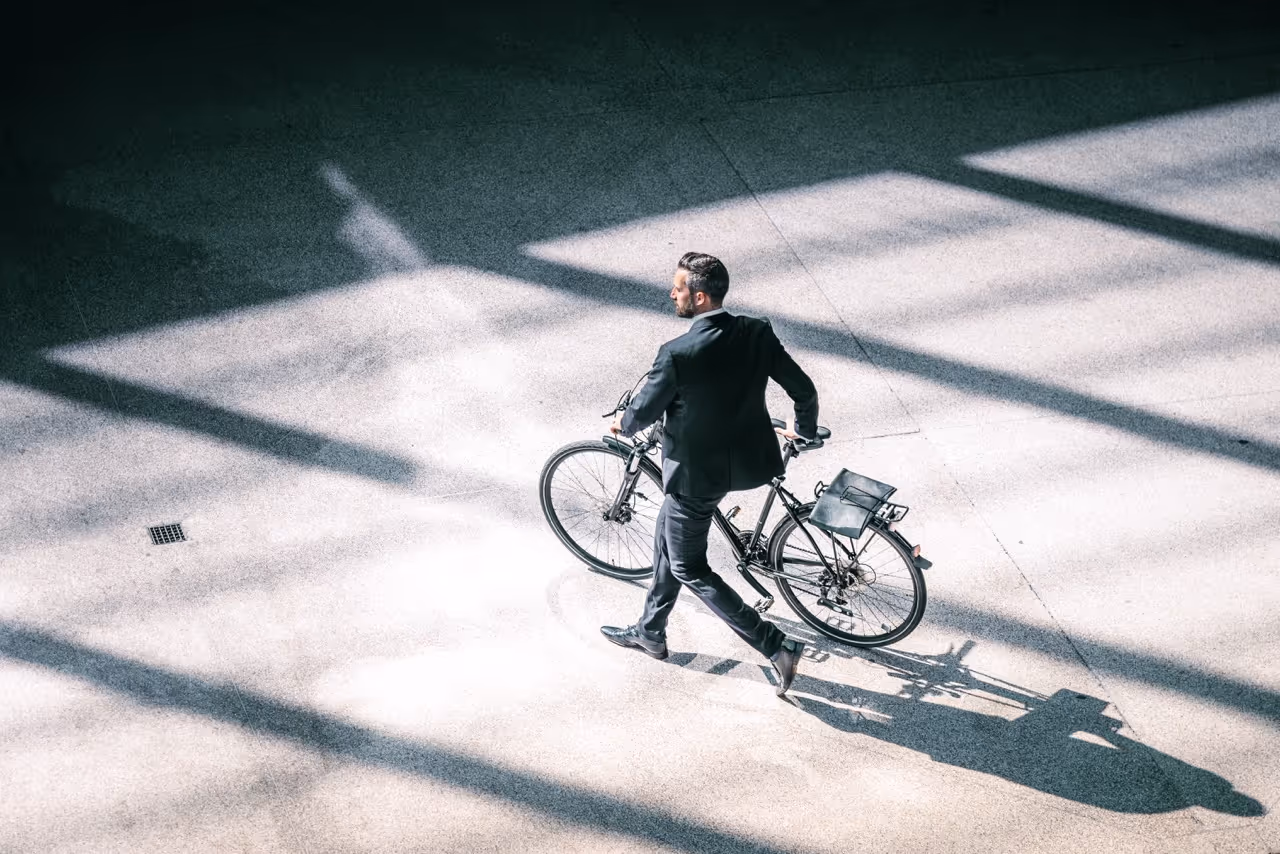 En mand iført jakkesæt går med sin cykel, hvilket illustrerer en unik kombination af formelt tøj og en afslappet aktivitet.