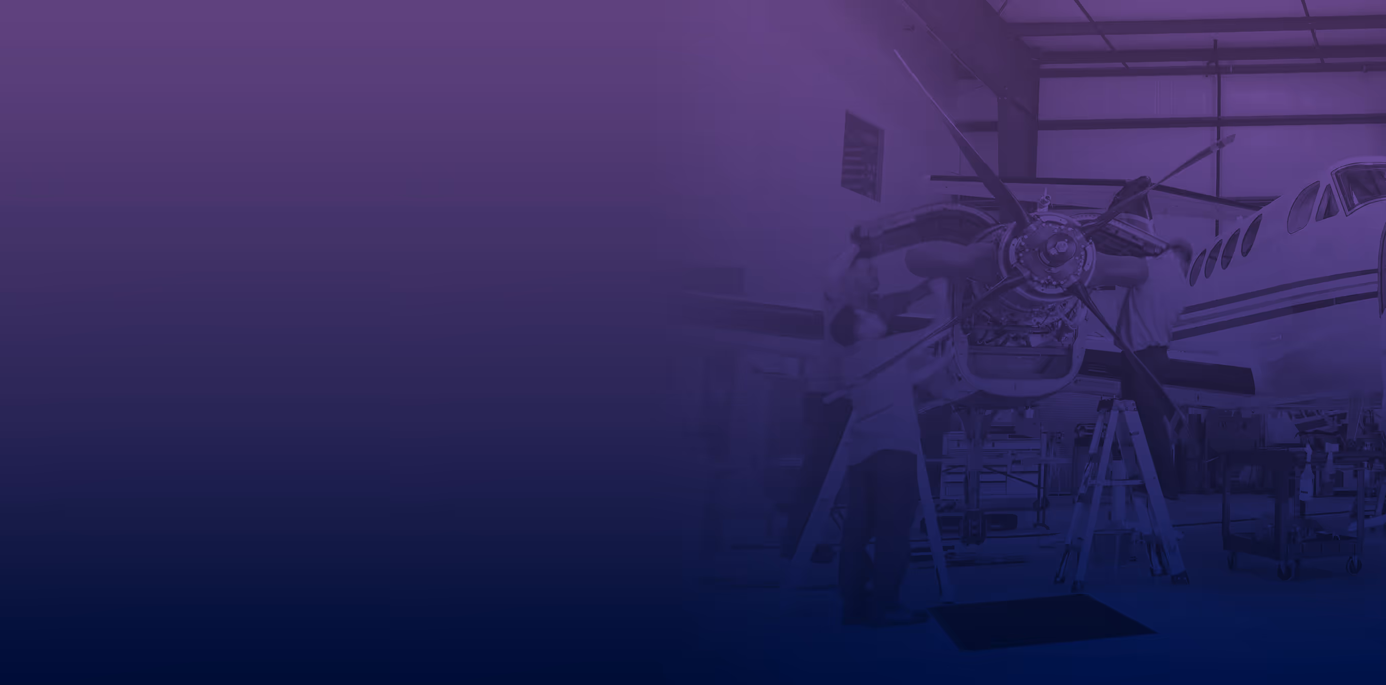 Three people working on the engine of a small aircraft inside a hangar.