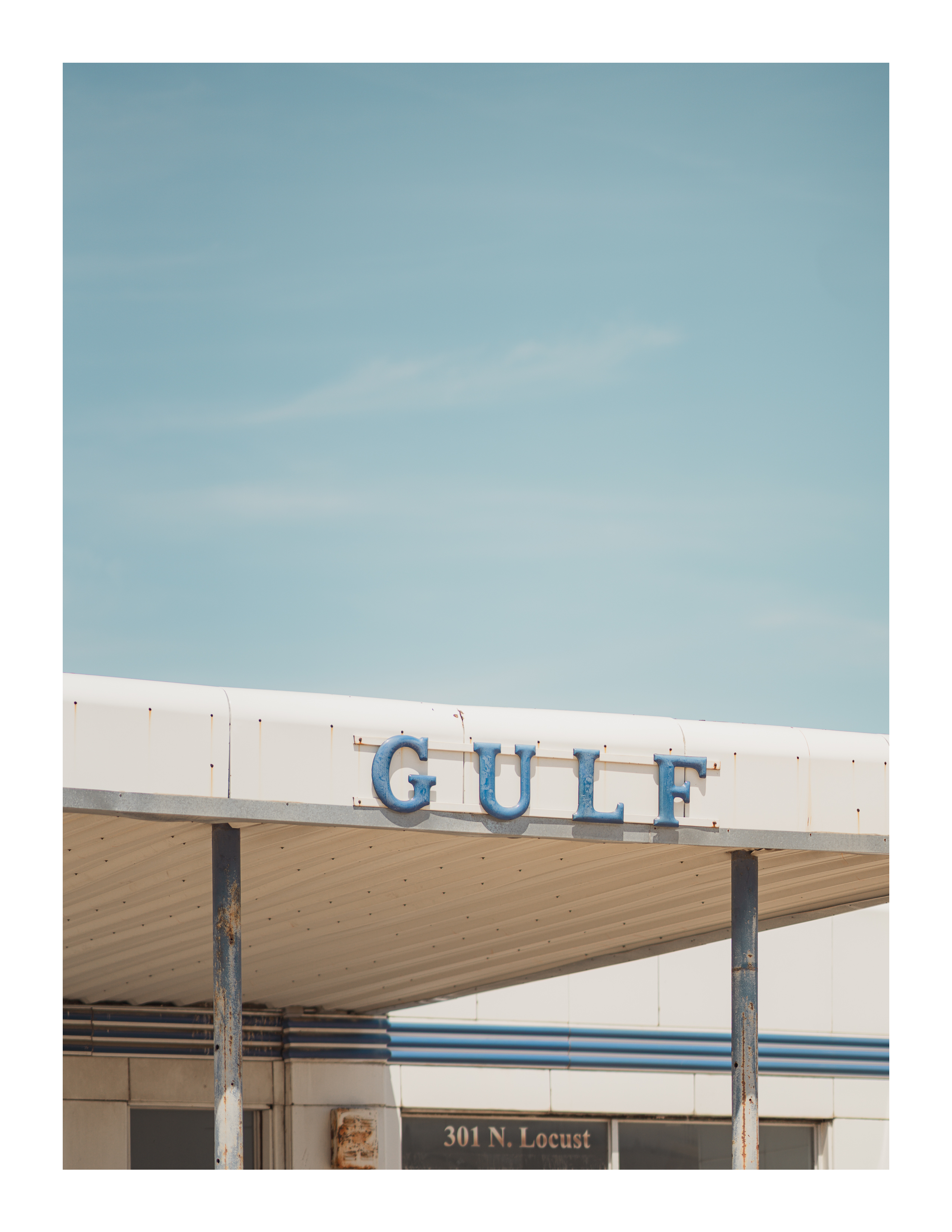 Rusted Gulf gas station awning with blue lettering and a soft sky in Denton, Texas