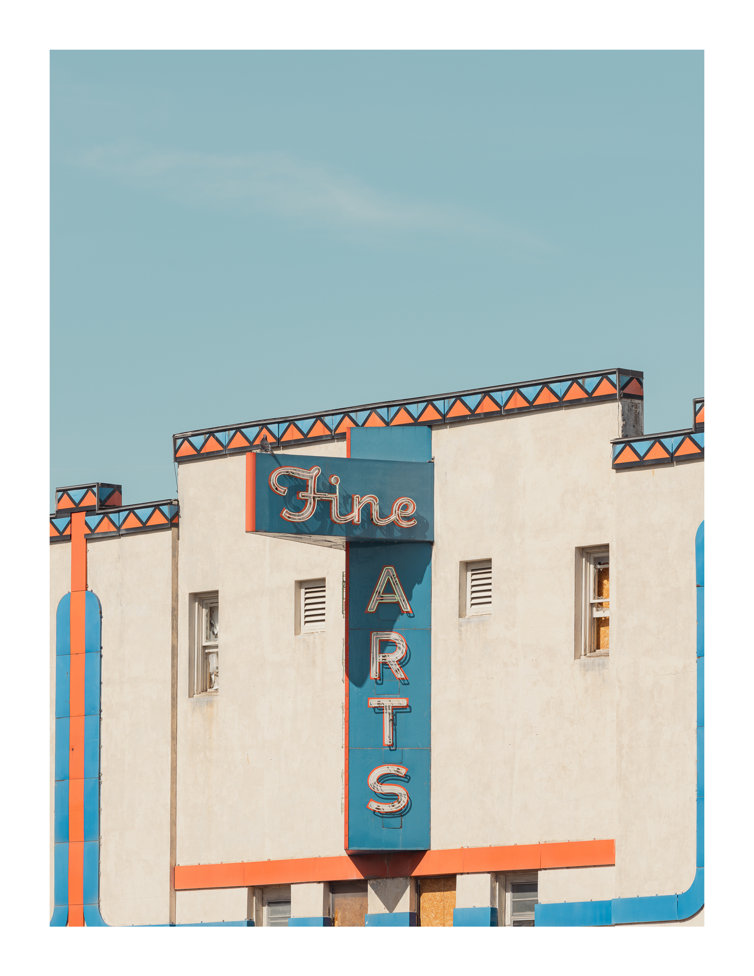 Vintage “Fine Arts” theater sign on stucco building with orange and blue trim under pale sky