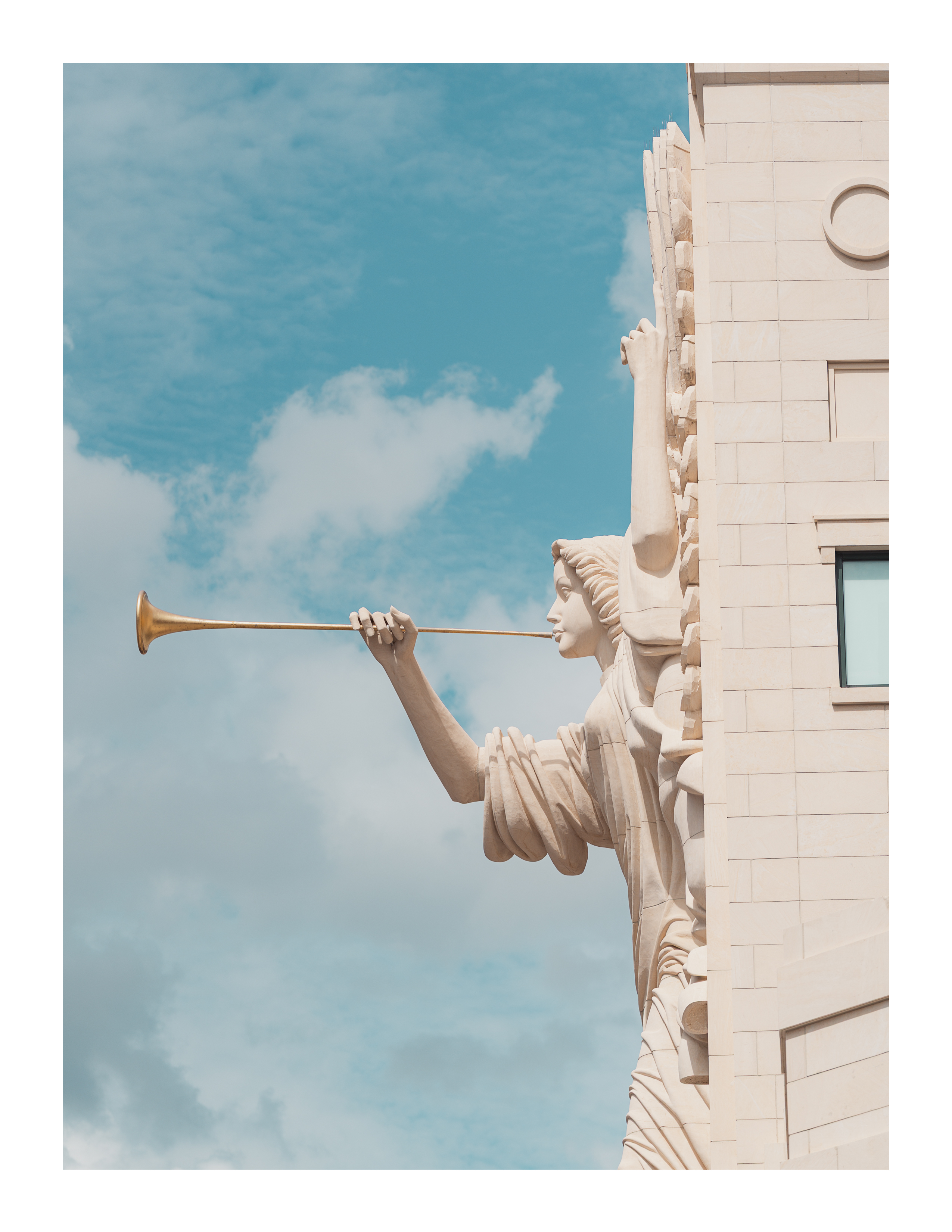 Sculptural angel with trumpet on limestone building façade against blue sky