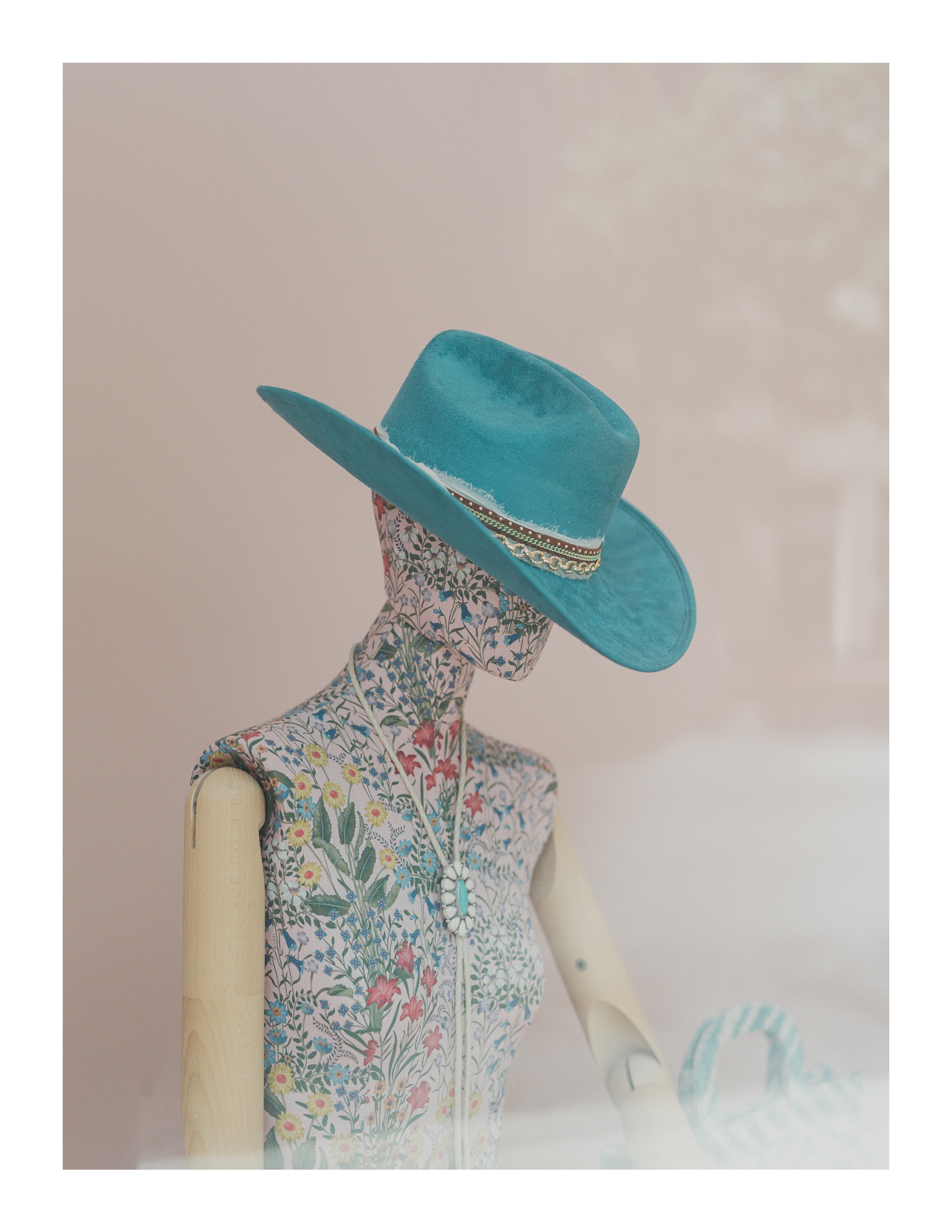 Storefront mannequin in floral print and turquoise hat, photographed through glass
