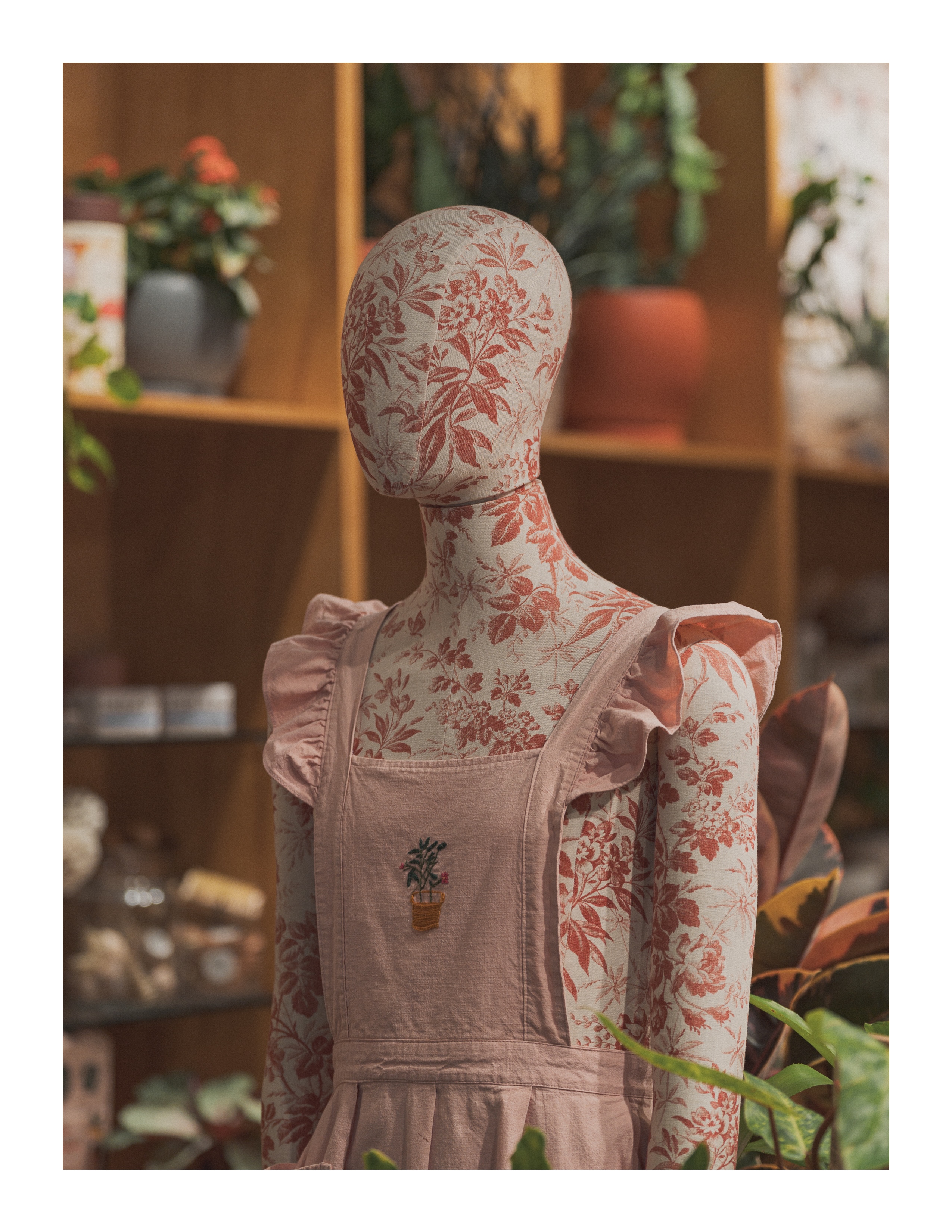 Floral mannequin in pink overalls surrounded by houseplants in a shop interior