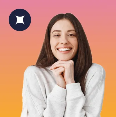 Smiling young woman with long brown hair wearing a light gray sweater, posing with hands clasped under her chin against a gradient pink to orange background.