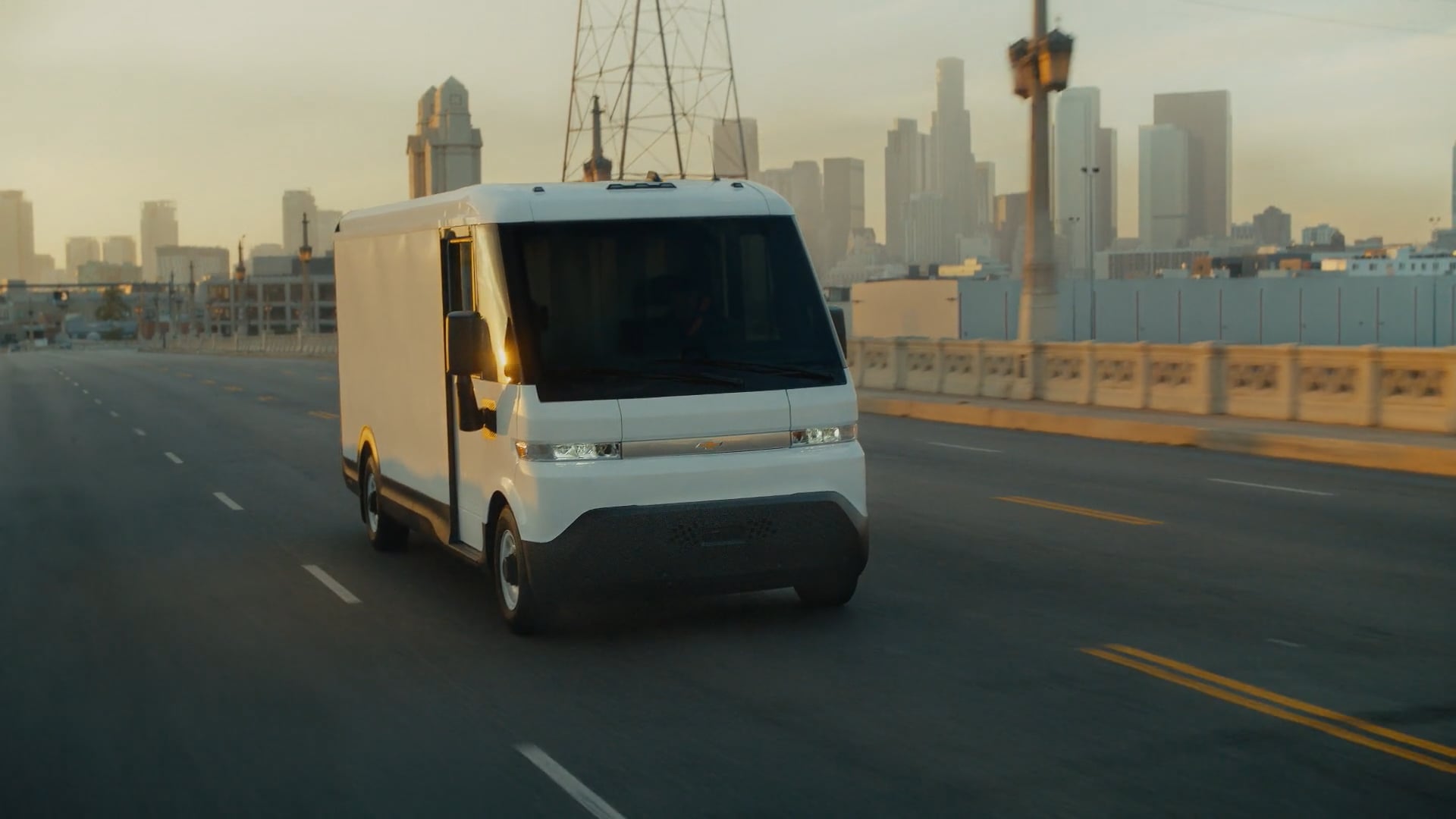 White autonomous delivery vehicle on bridge with city skyline in background