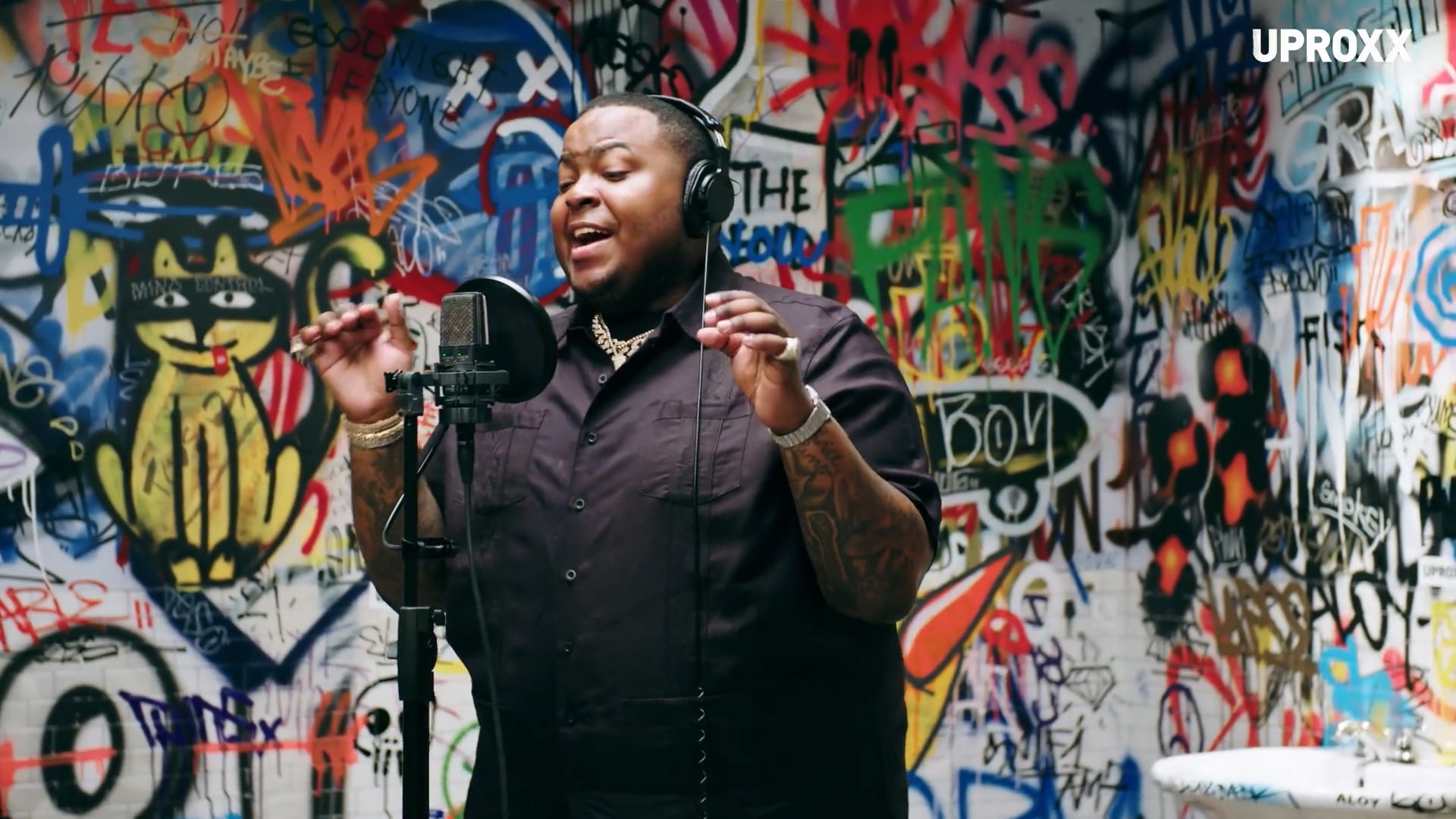 Person wearing headphones singing into microphone against colorful graffiti wall background