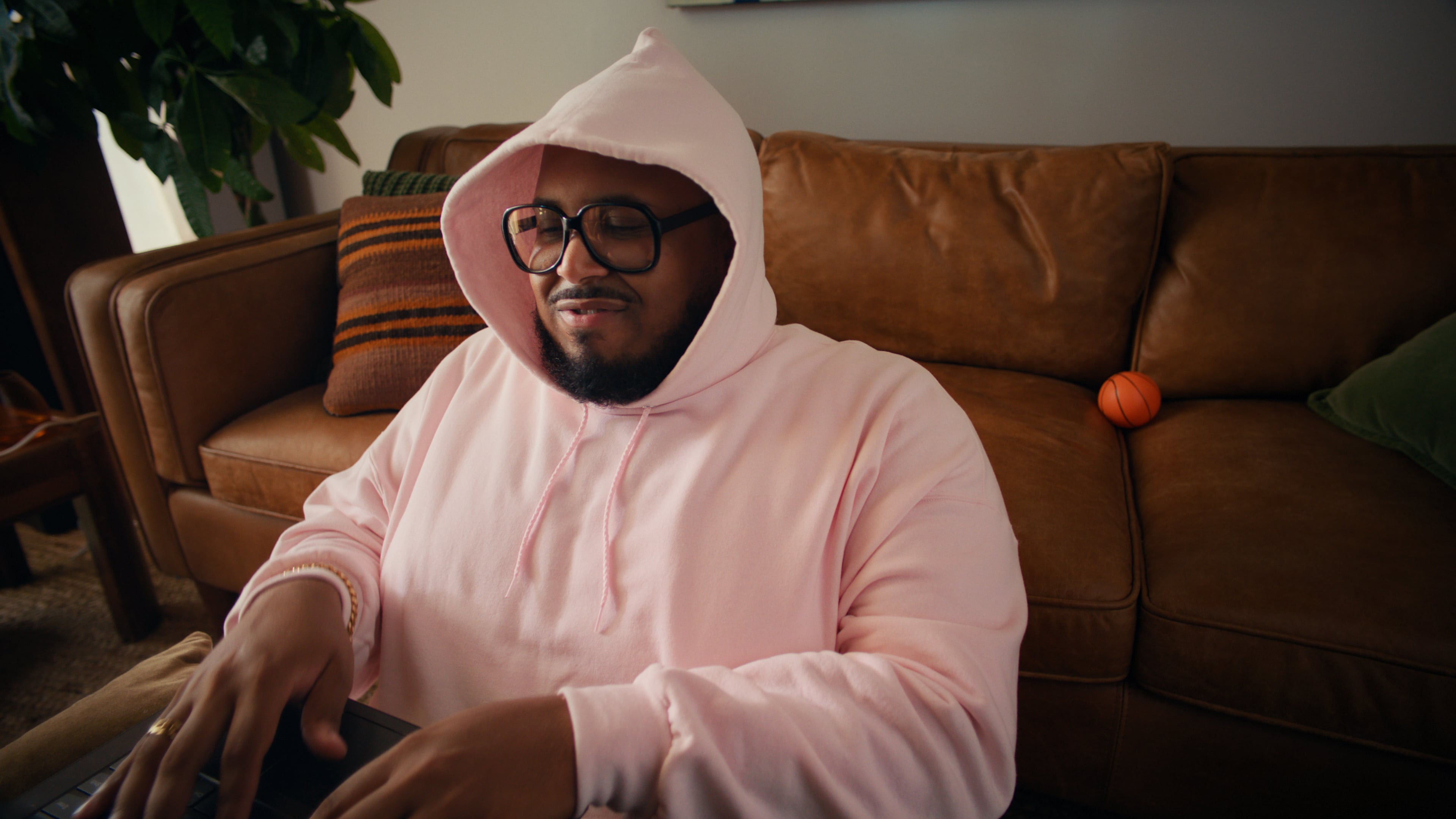 Man in pink hoodie and glasses sitting on brown leather couch