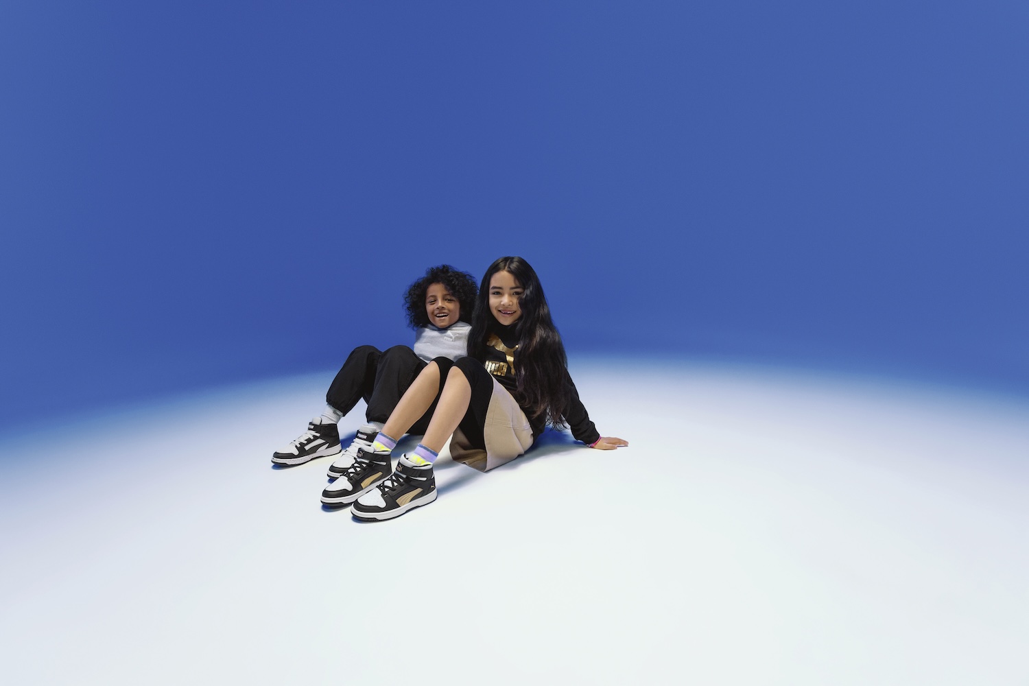 Two young women sitting together on white ground against blue sky background