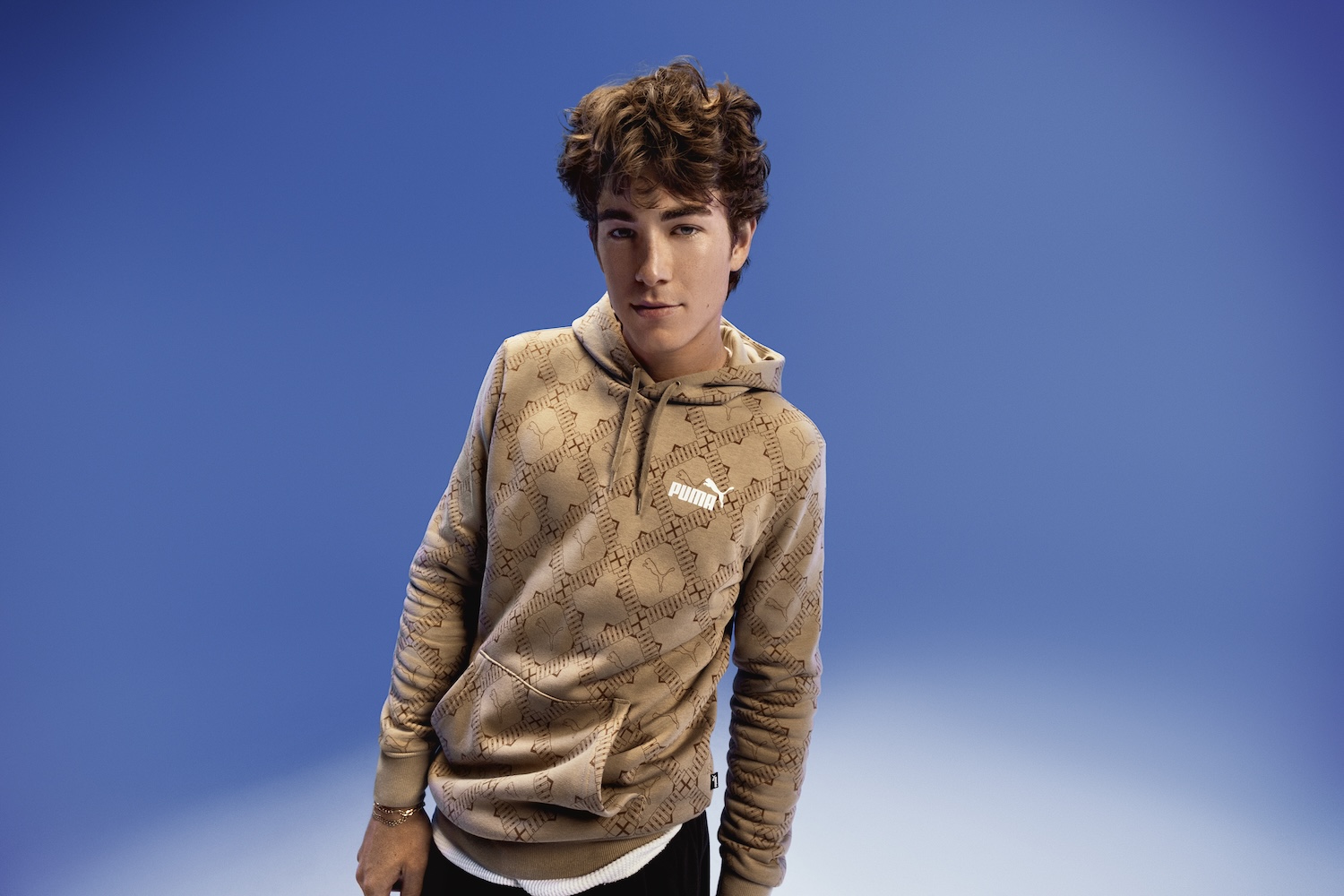 Young male model wearing beige patterned hoodie against blue background