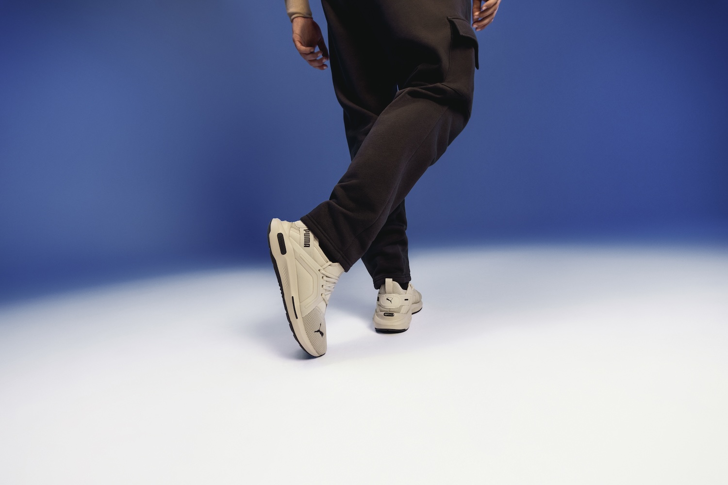 Person wearing cream sneakers and black pants against blue background