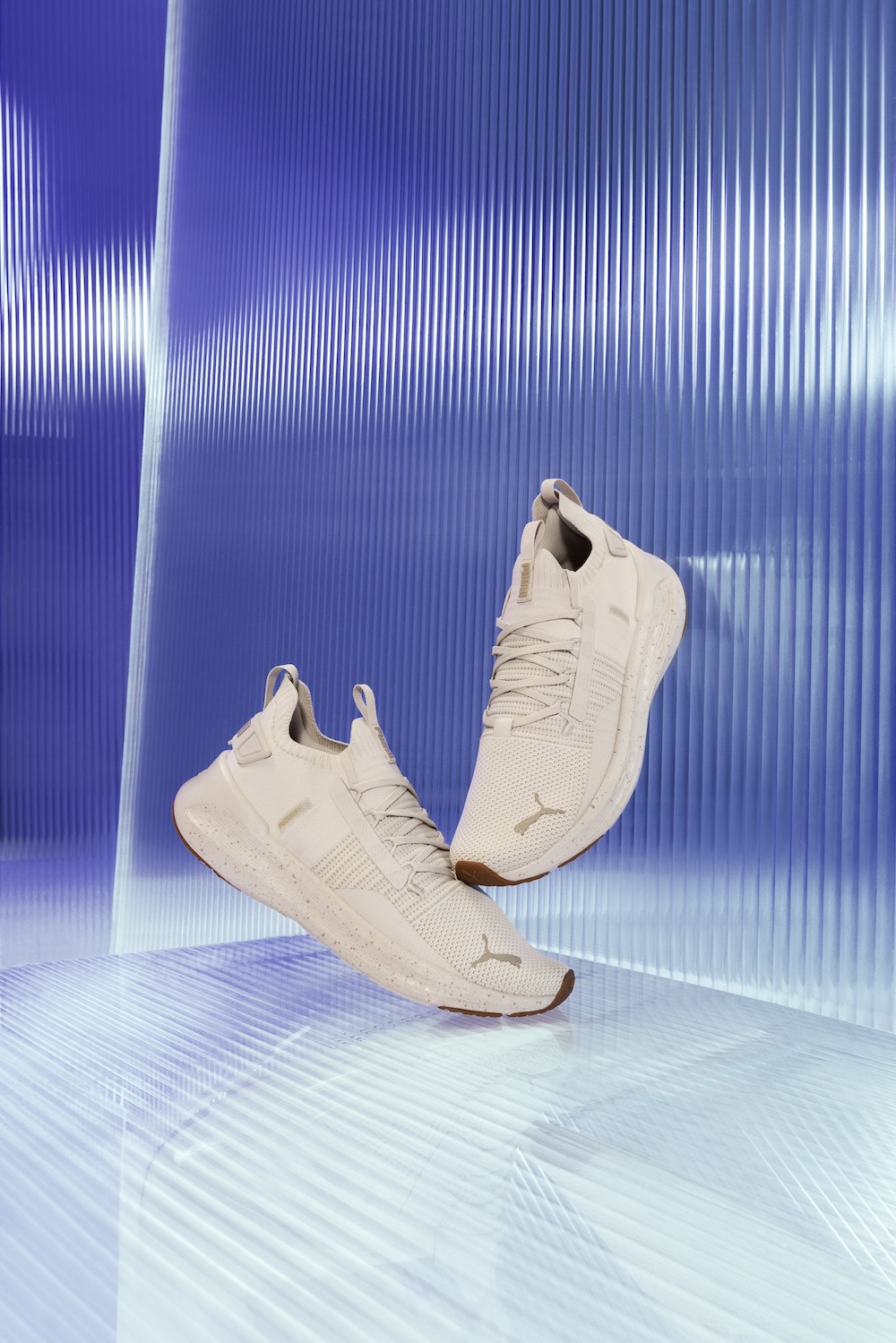 Three cream-colored Puma sneakers displayed against blue textured background with white vertical lines.