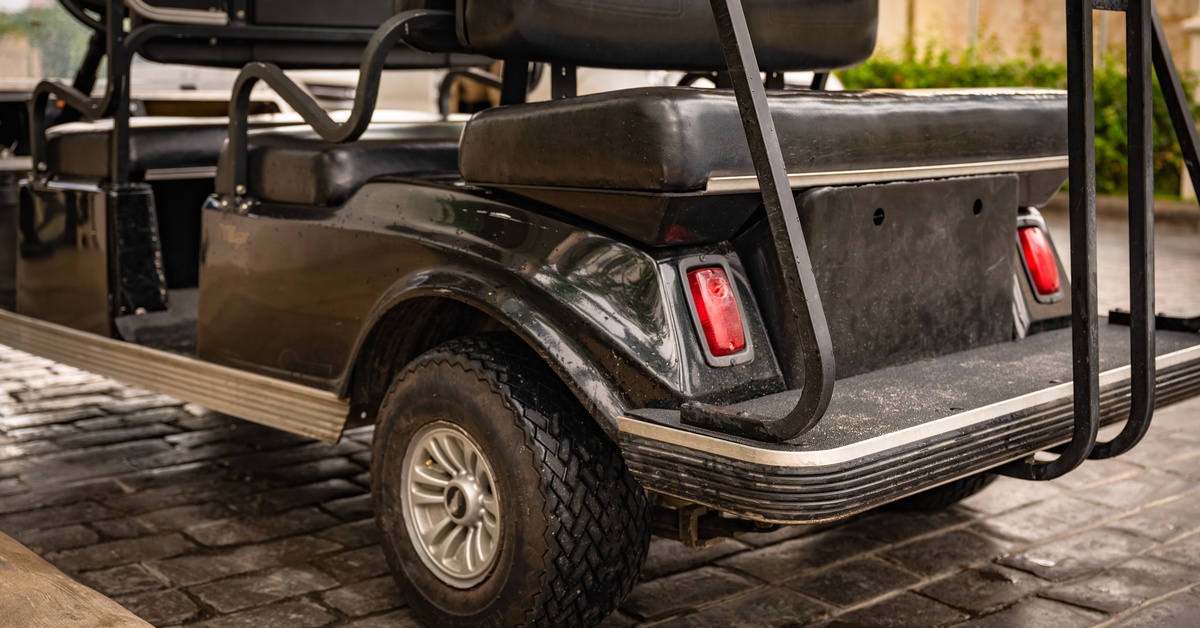 Close-up to the left back tire of a modern black golf cart with small red lights parked on a road with black tiles.