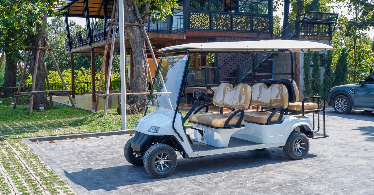 Electric golf cart with six seats covered in protective plastic, parked in front of a home surrounded by nature.