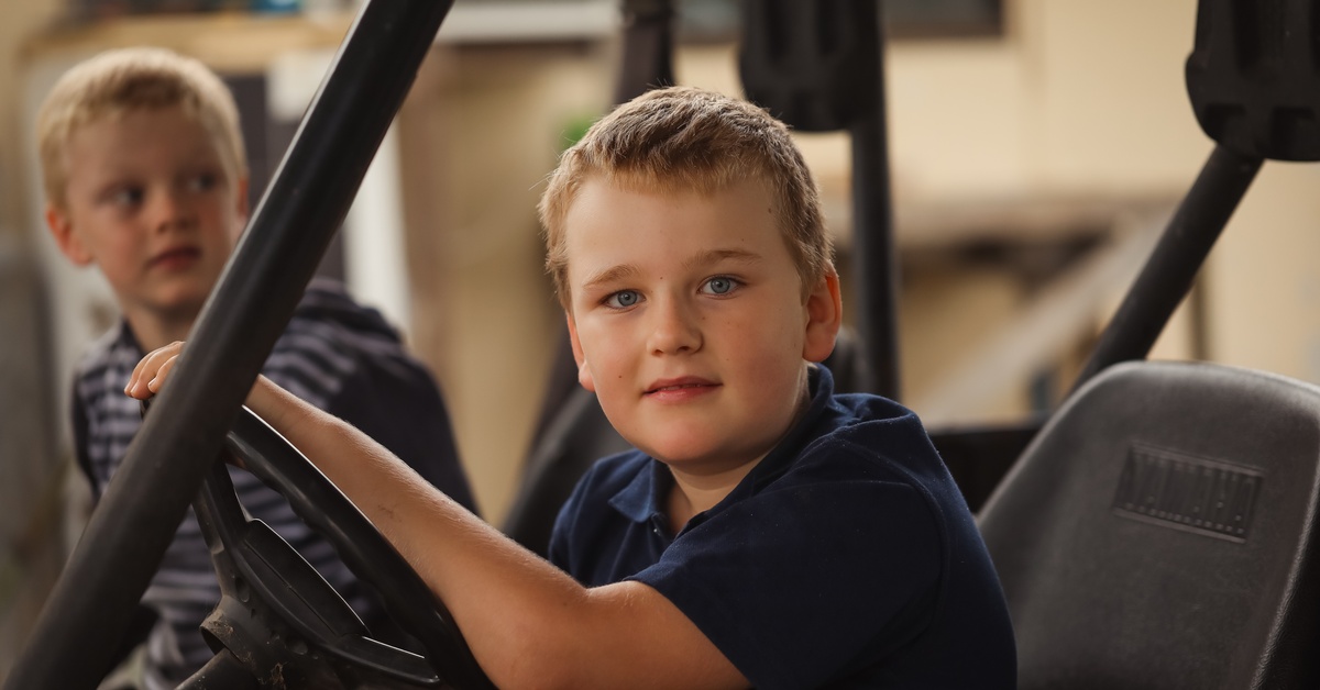 Boy behind the wheel of a golf cart on the driver's seat with another boy on his side, parked in front of a home.
