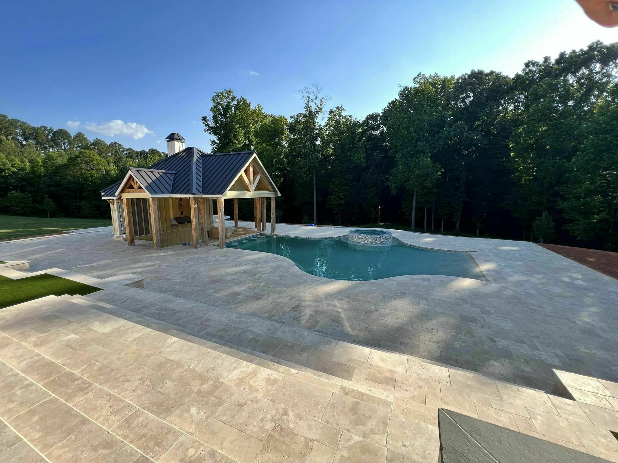 Travertine pavers surround a modern swimming pool with a beautiful lake in the background.