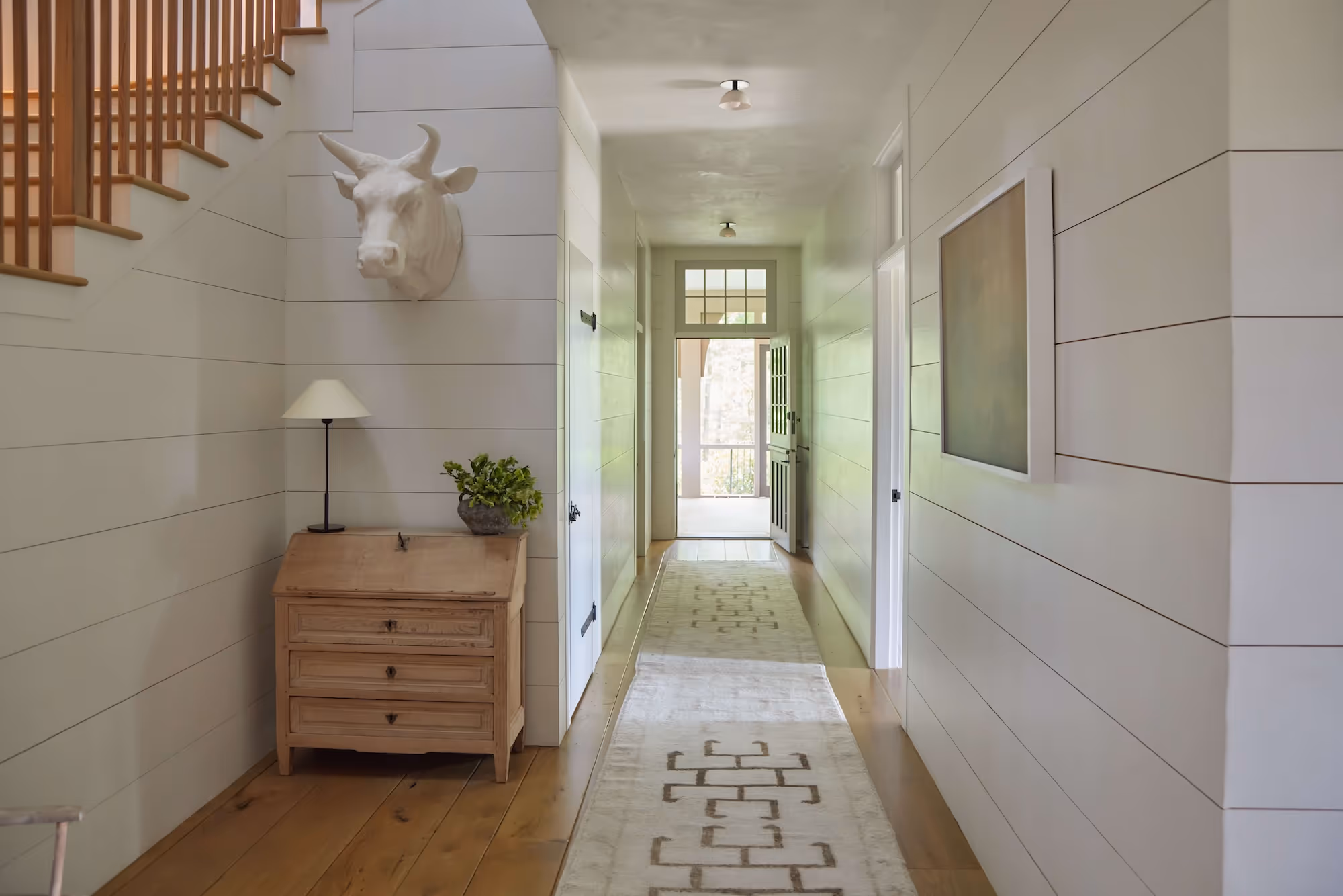 A bright, shiplap-lined hallway layered with a soft, subtly patterned Moattar runner, bringing warmth and elegance to a classic Southern entry.