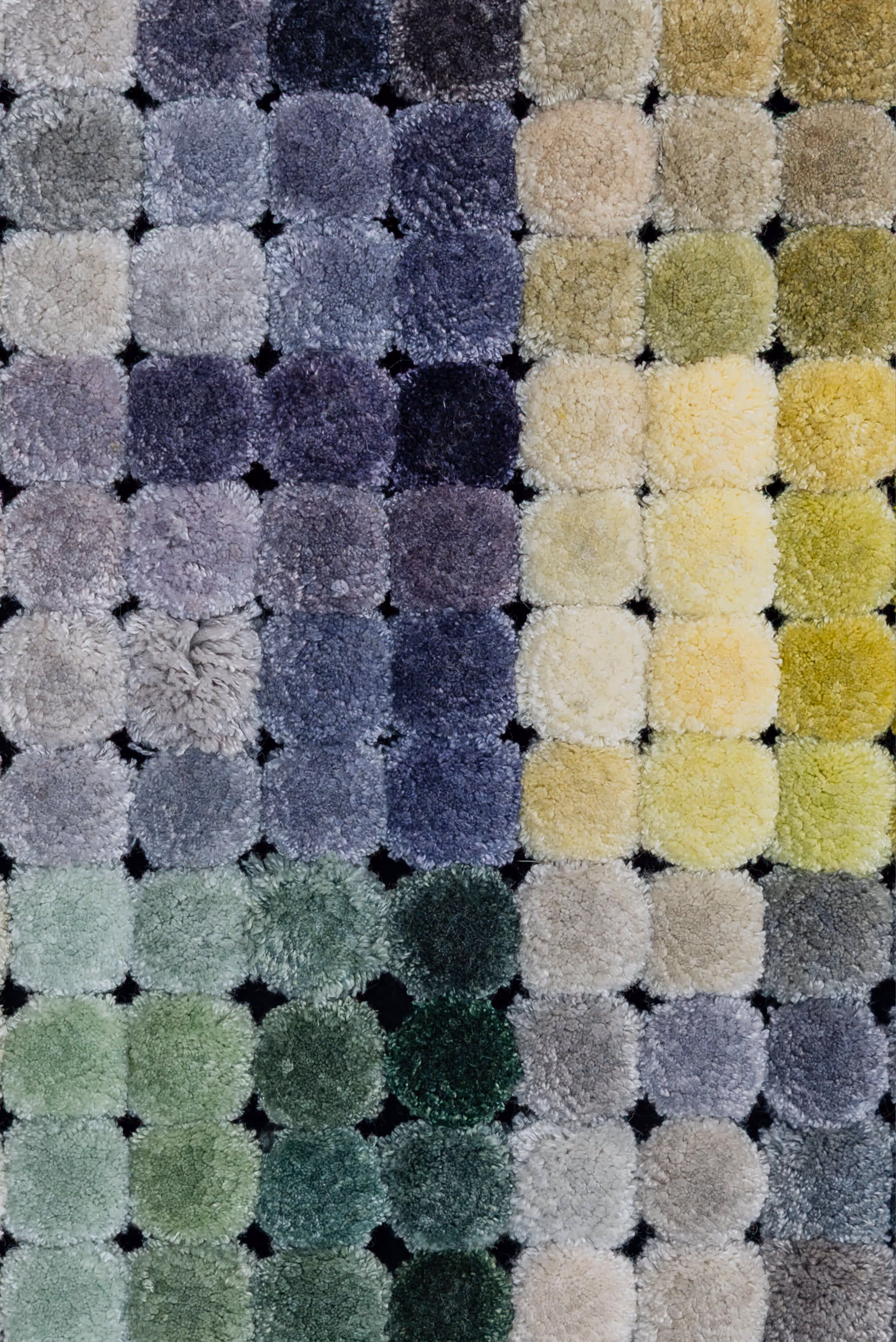 Close-up of a textured fabric sample board with square swatches in gradient shades of green, yellow, grey, and purple.