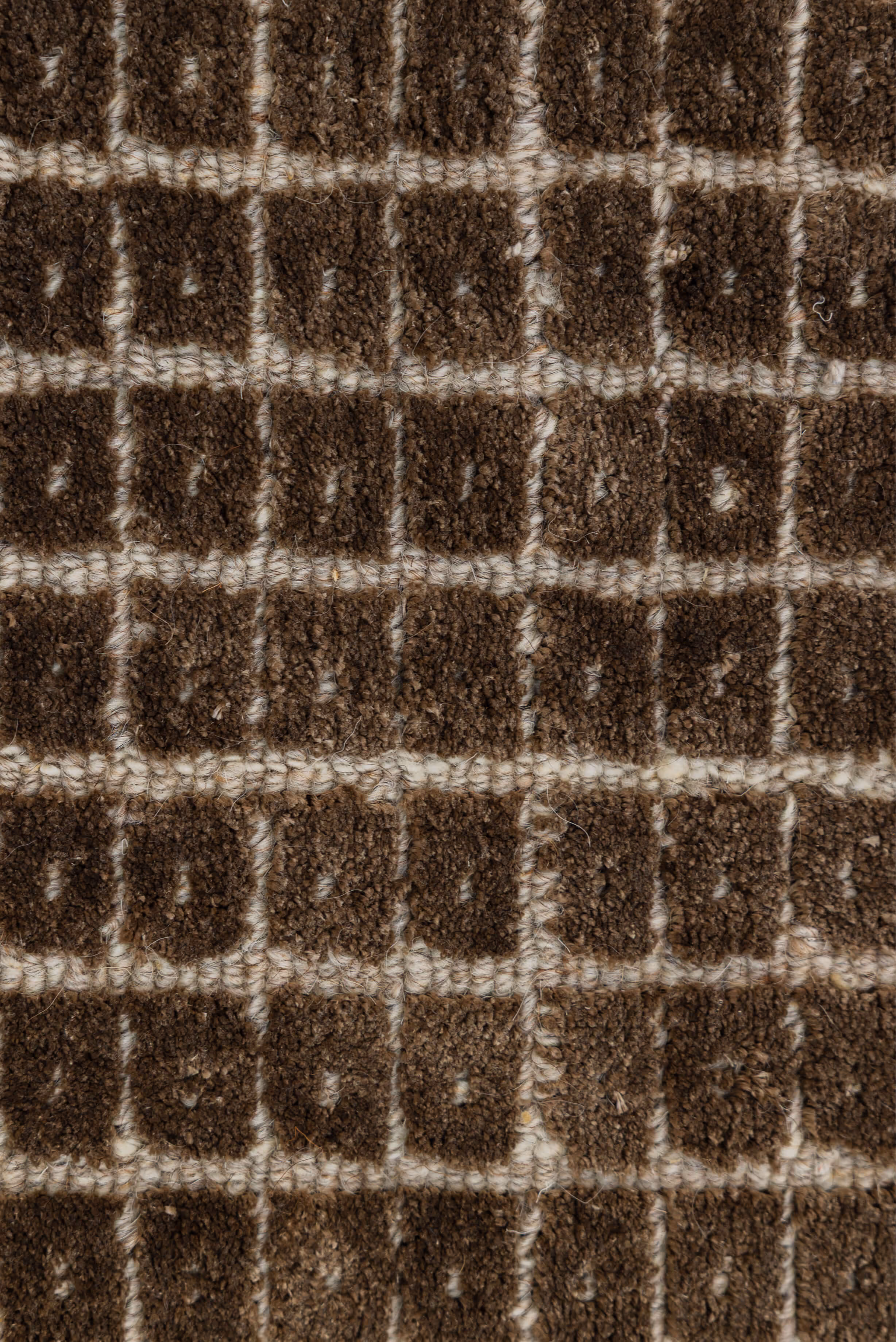 Close-up of a textured woven fabric with dark brown square patterns separated by lighter beige grid lines.