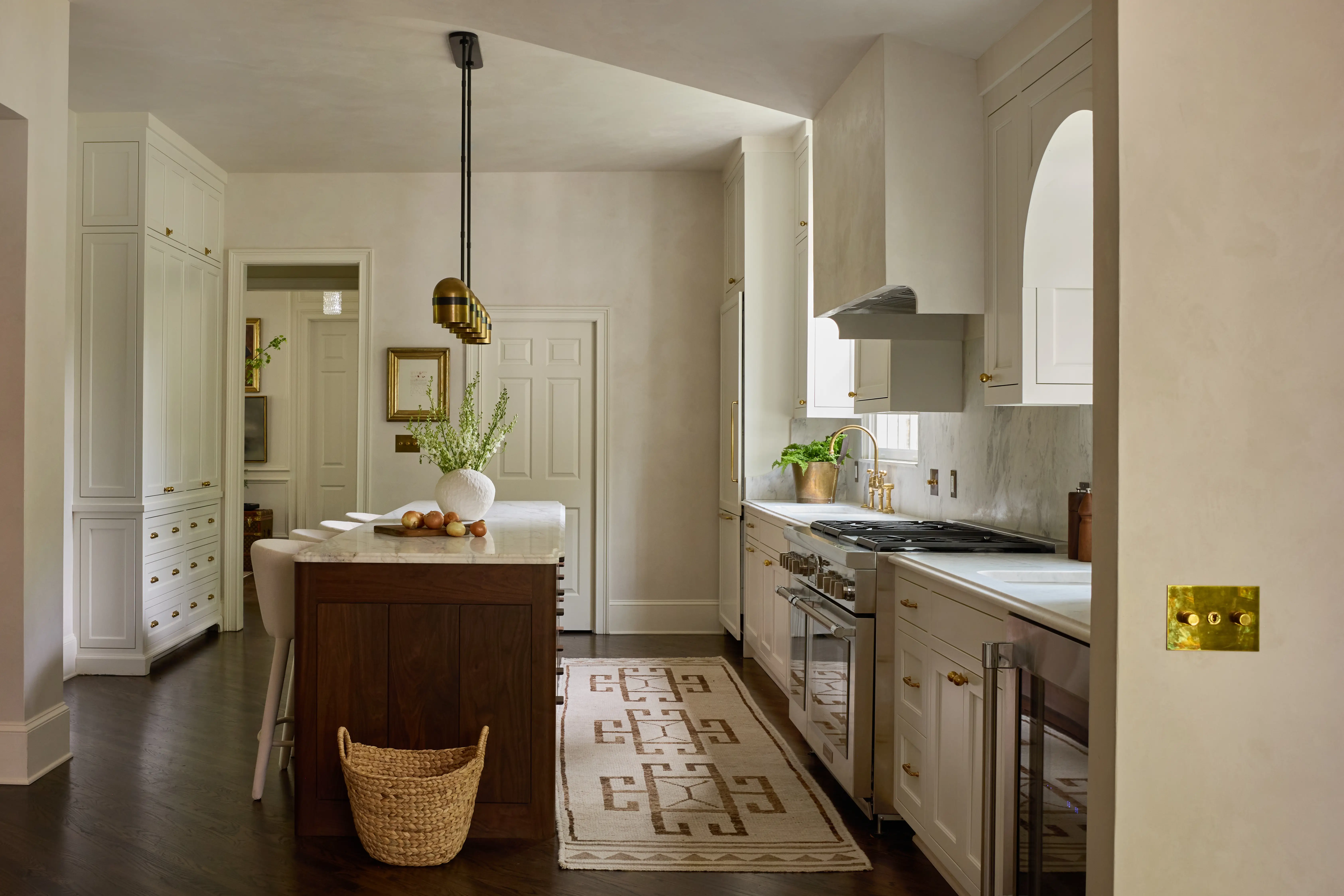 Modern kitchen with white cabinets, wooden island, brass light fixtures, and a patterned runner rug.